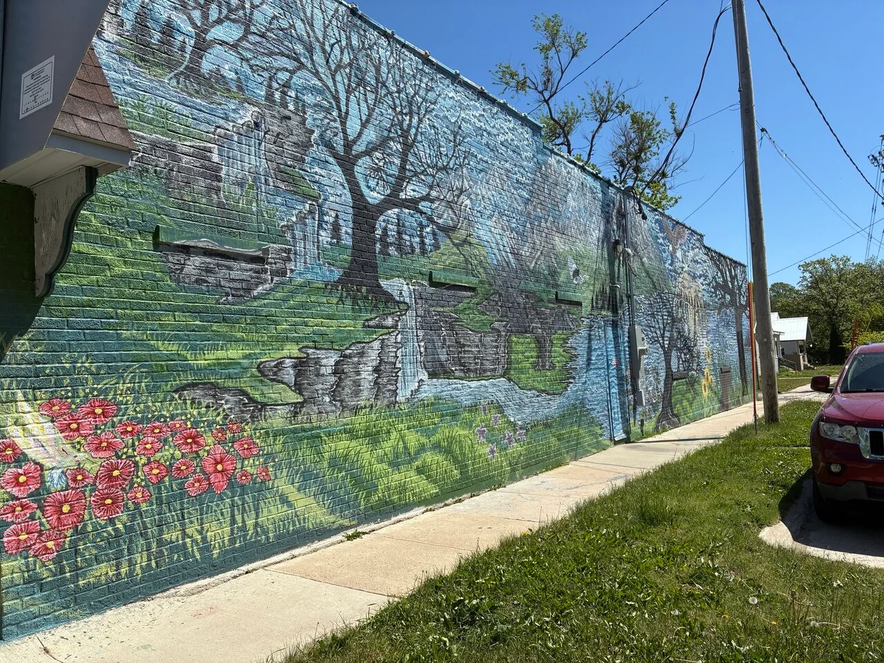 Colorful mural depicting nature with flowers and a waterfall on a brick wall.
