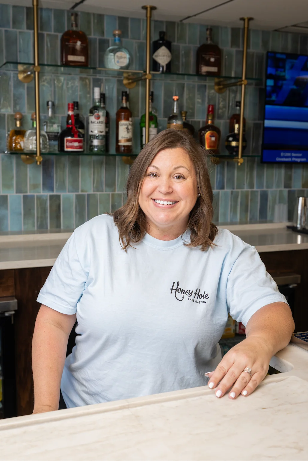 Smiling bartender at Honey Hole restaurant with a bar backdrop.