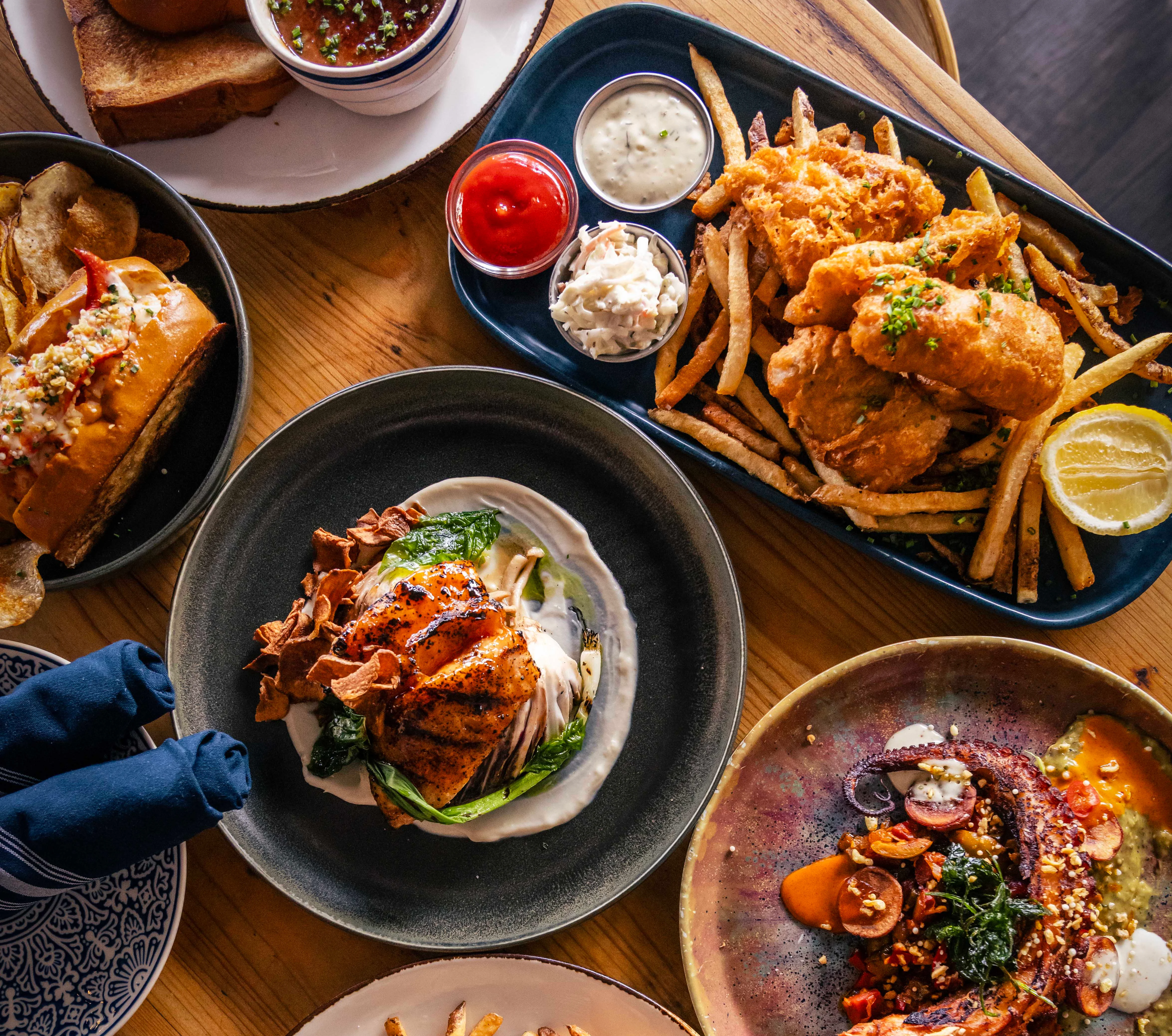 A variety of delicious dishes including seafood, burgers, and fries on a wooden table.