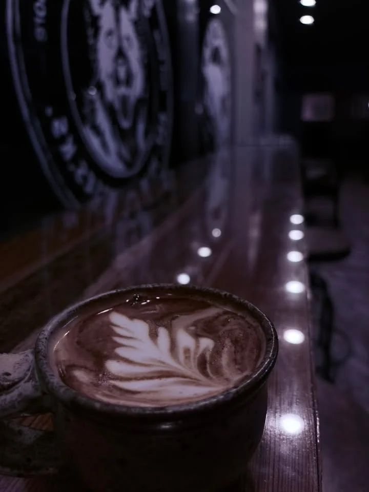 A close-up of a latte art in a ceramic cup on a wooden counter, surrounded by low lighting.