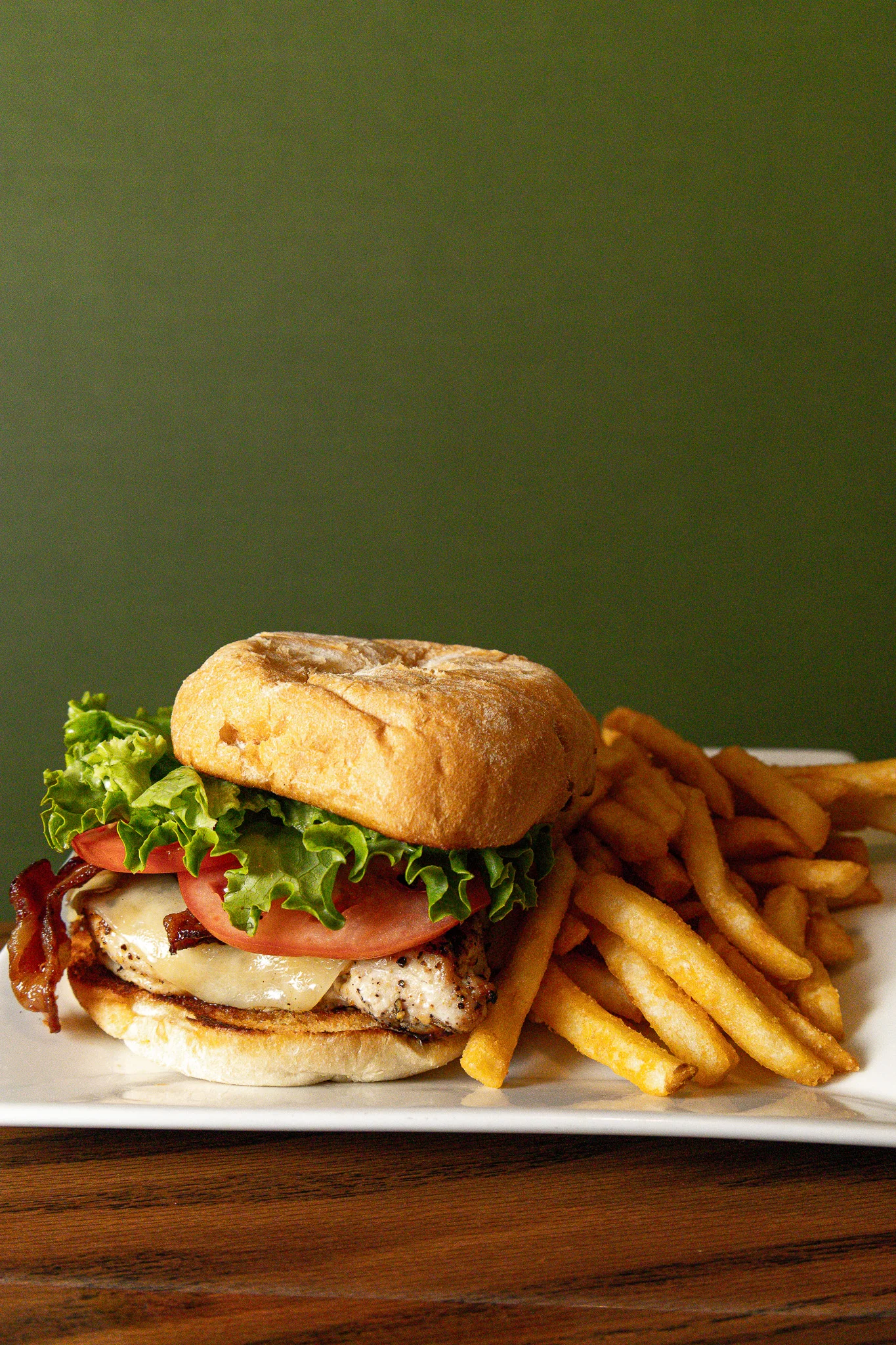 Grilled chicken sandwich with bacon and fries on a white plate
