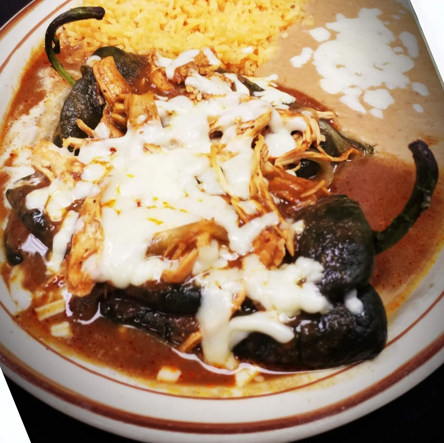 Authentic Chile Poblano at El Charro Mexican Grill in Radford - roasted Poblano pepper stuffed with cheese, topped with shredded chicken and melted cheese, served with seasoned rice and refried beans.