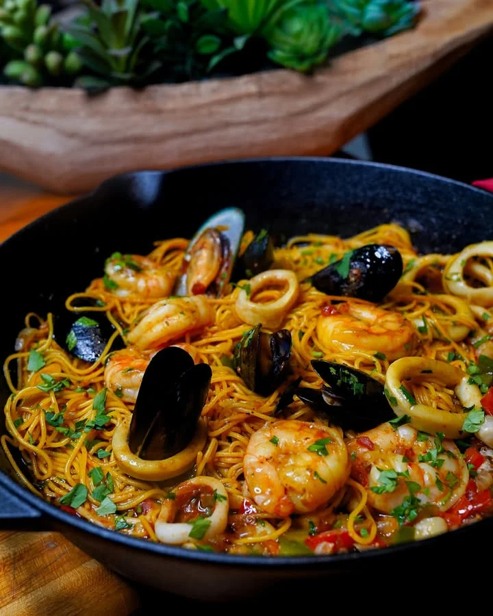 A delicious seafood pasta dish featuring shrimp, mussels, and calamari on a bed of noodles, garnished with fresh herbs.