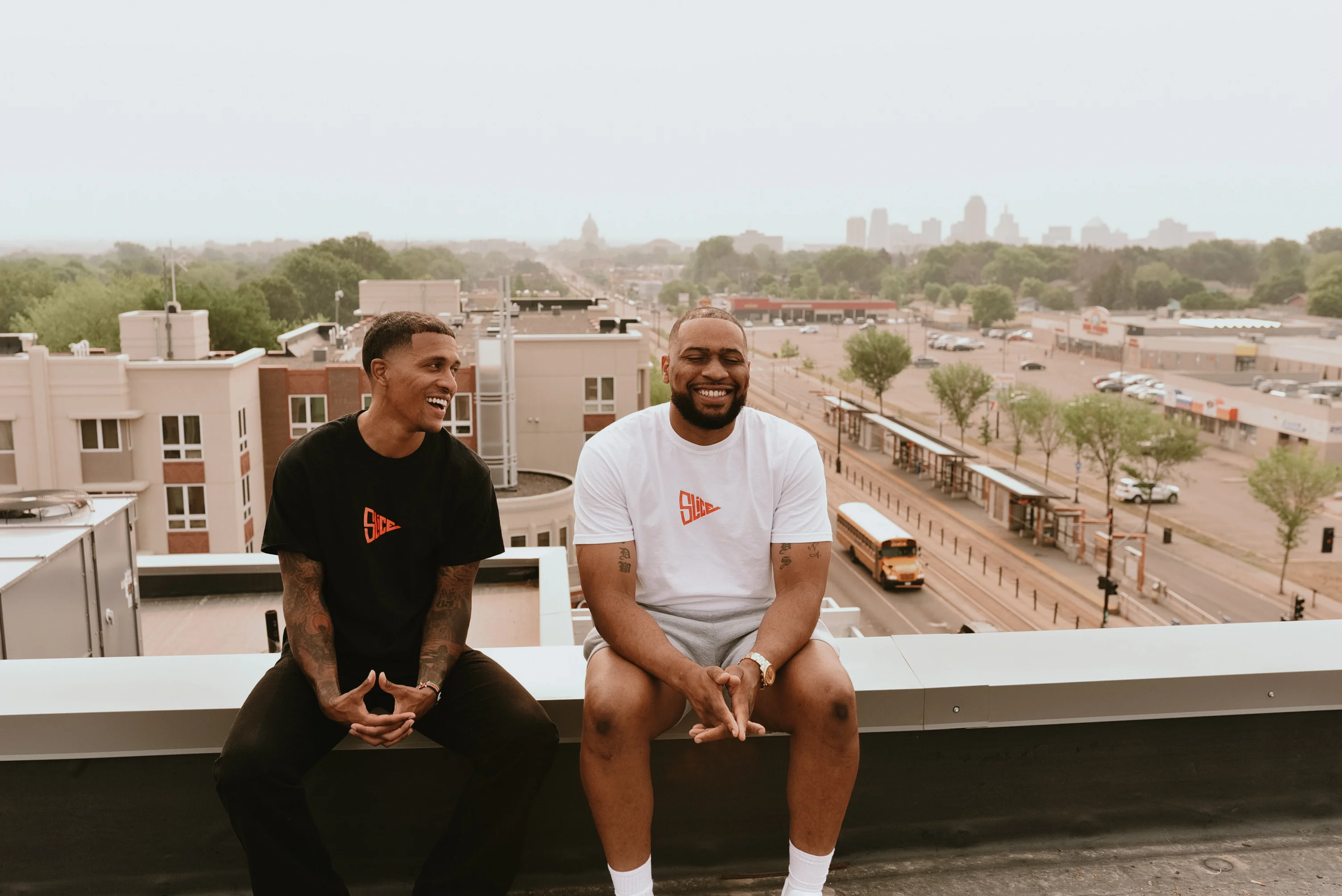 Two friends laughing on a rooftop with a city skyline in the background