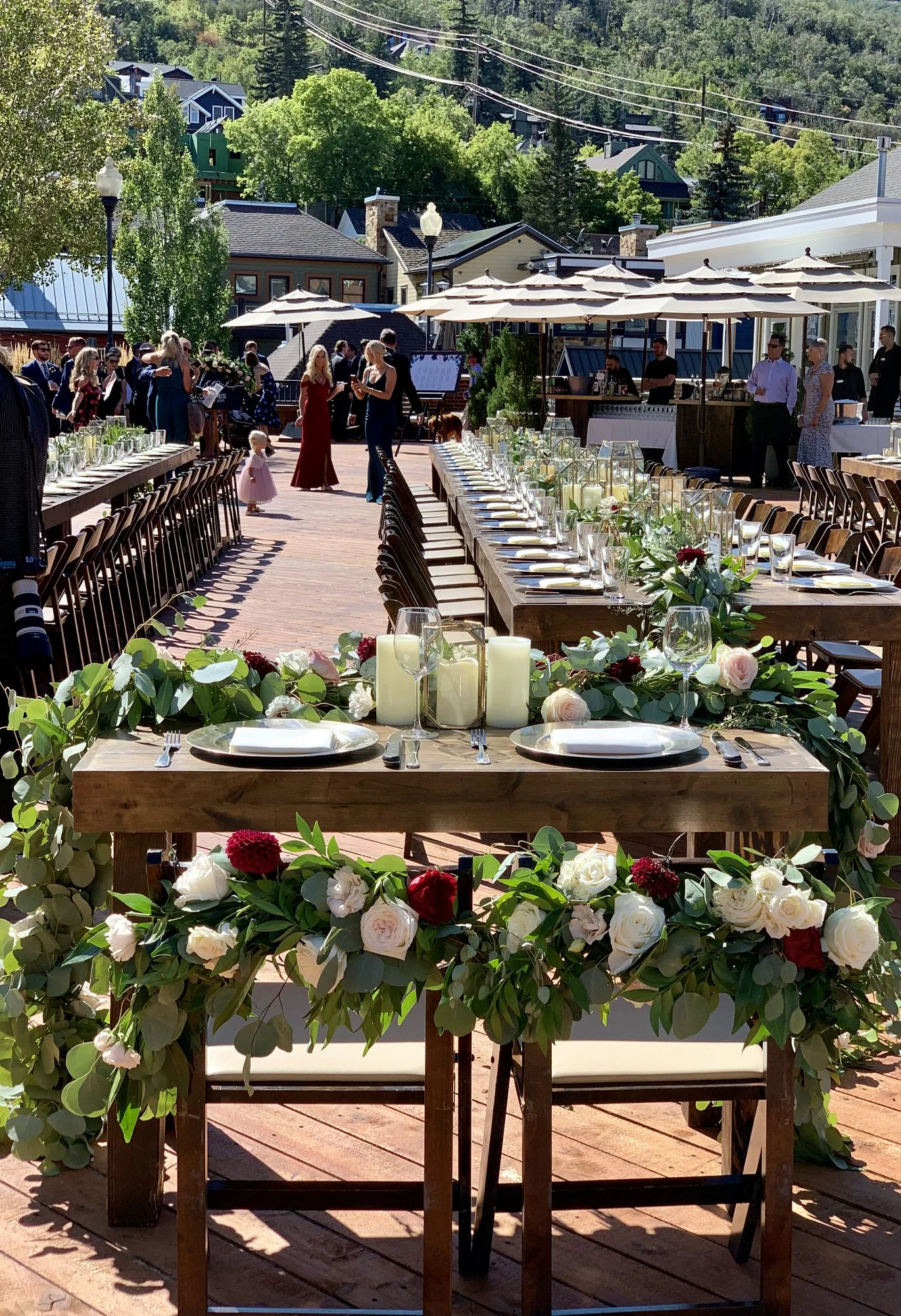 A beautifully arranged outdoor dining setup for an event, featuring long tables adorned with flowers and candles.