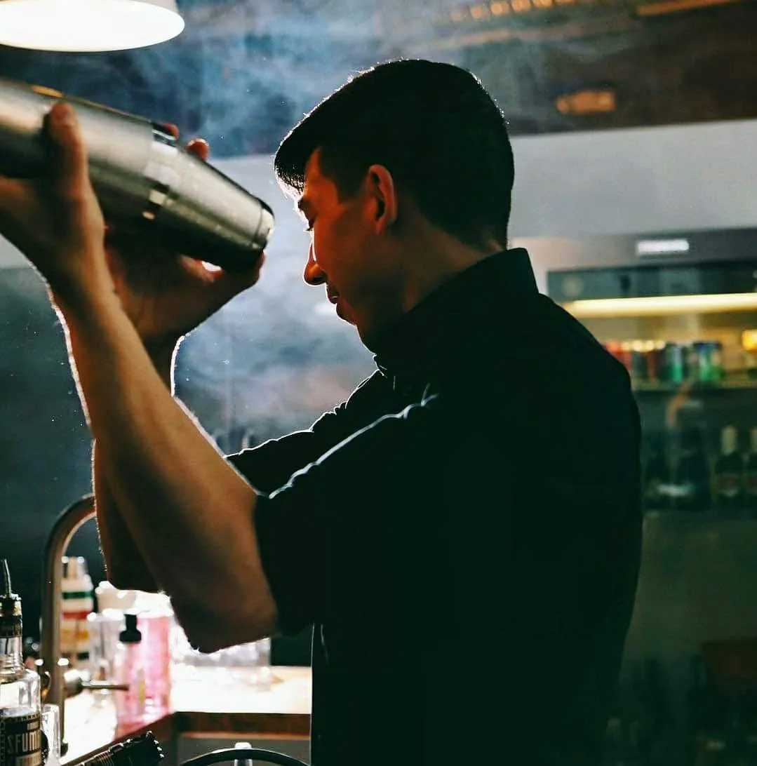 A bartender skillfully shaking a cocktail shaker in a dimly lit bar, creating a smoky ambiance.