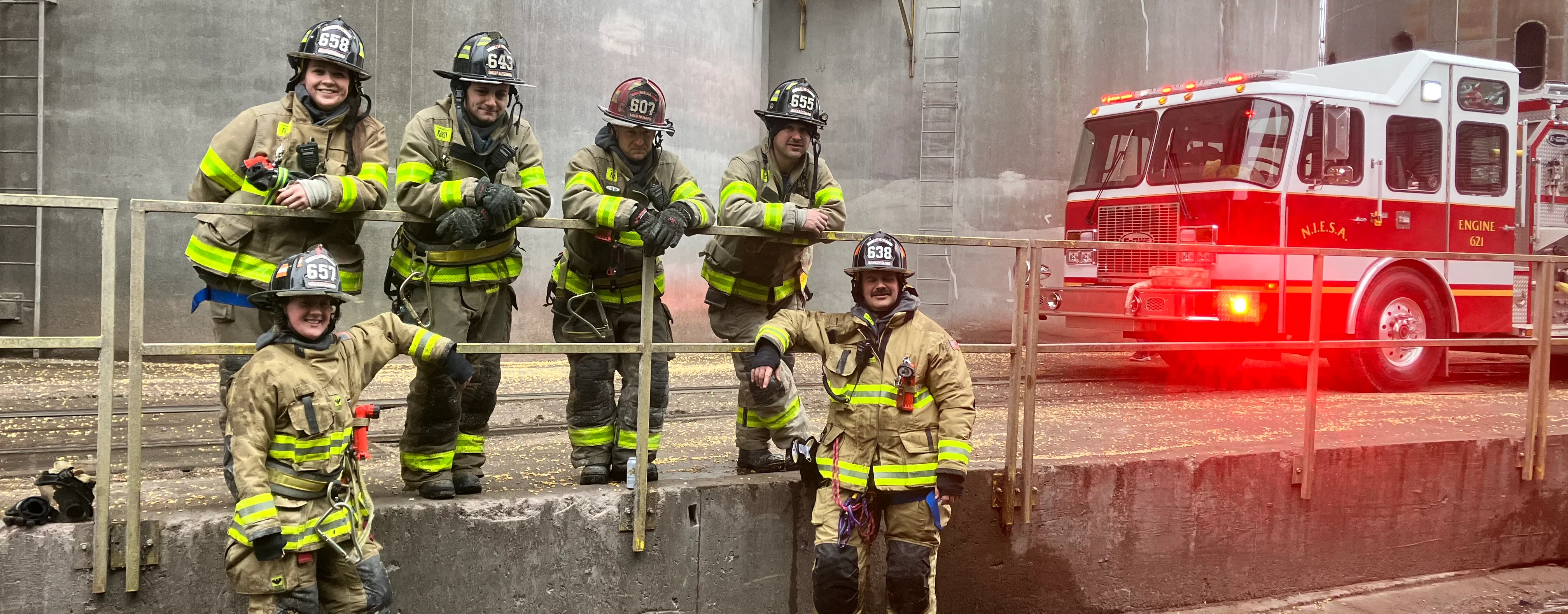 Group of firefighters posing with fire truck at industrial site