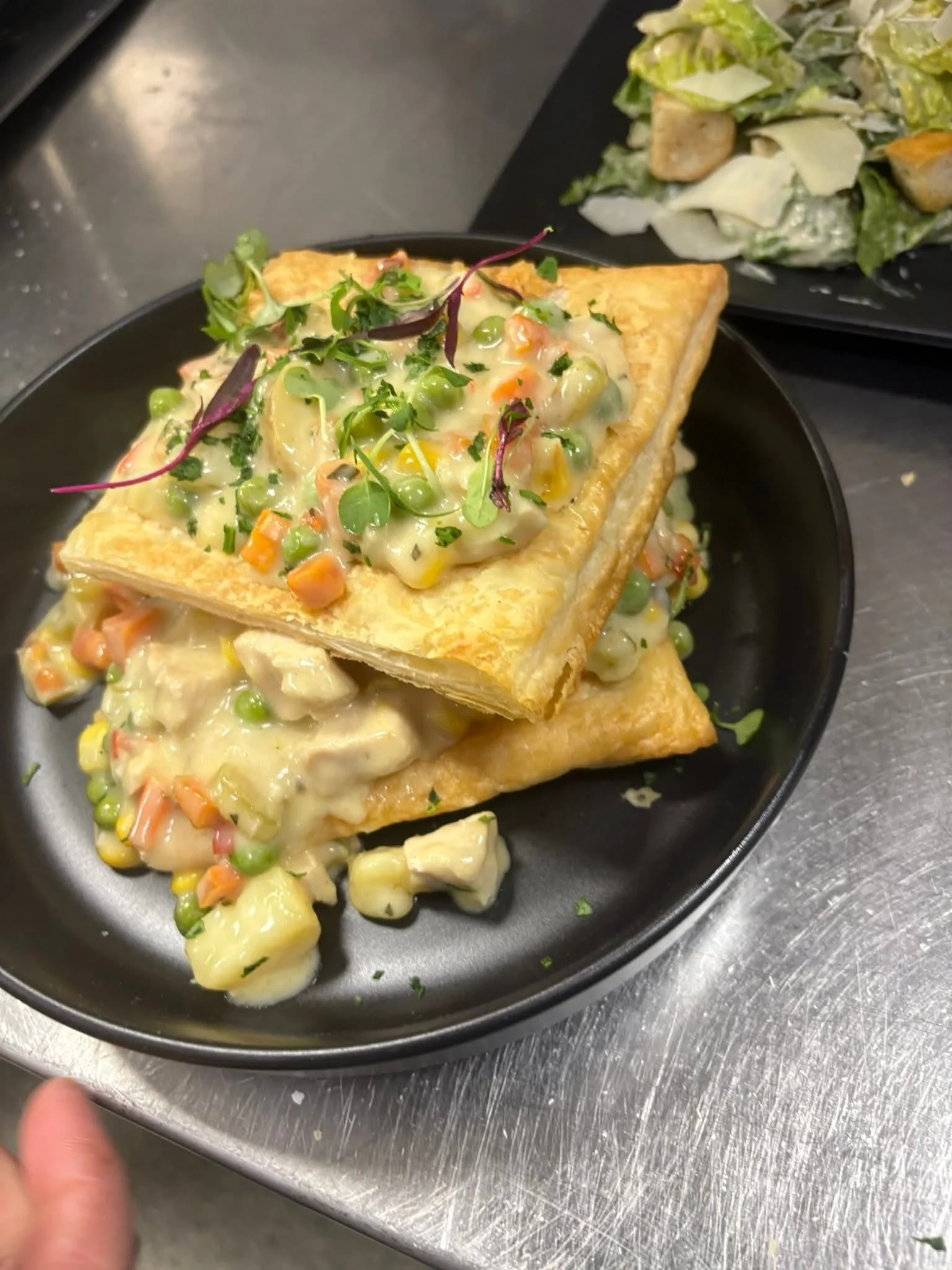 A plate featuring flaky pastry topped with a creamy mixture of vegetables and chicken, garnished with microgreens.