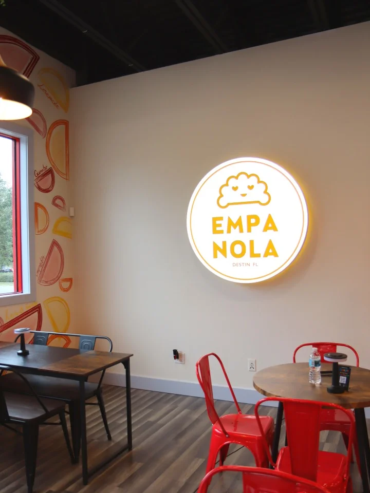 A dining area showcasing a prominent illuminated sign that reads 'EMPANOLA', with modern furniture and a cozy atmosphere.