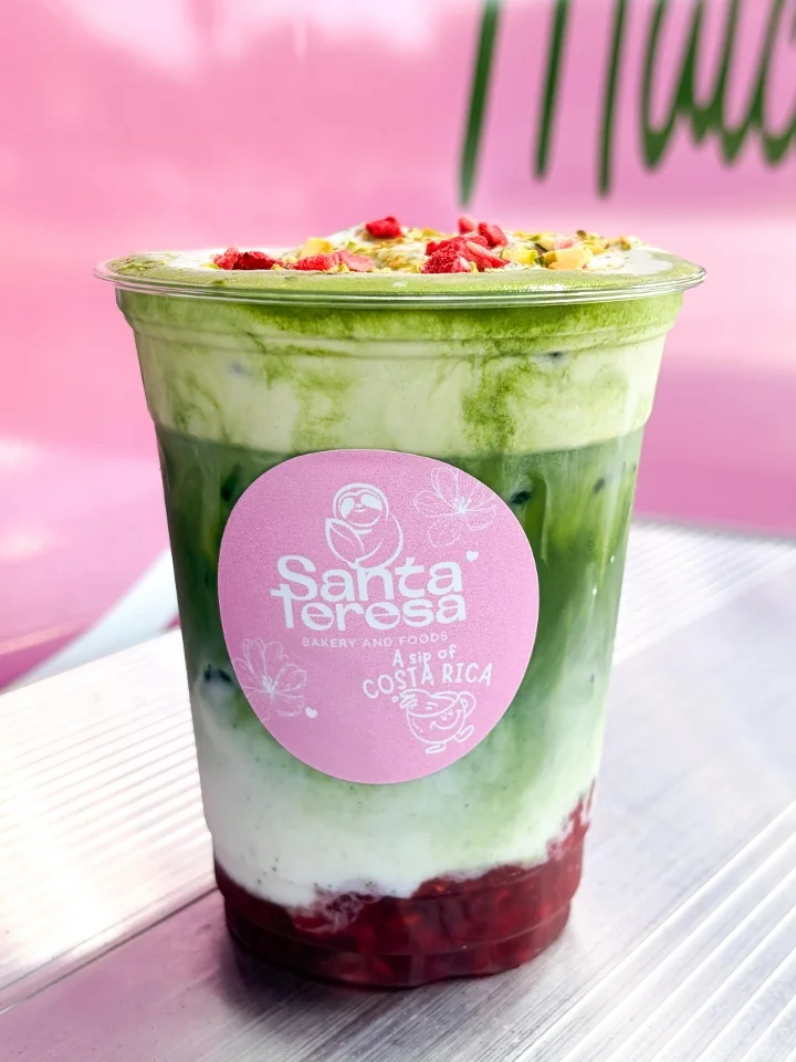 A similar layered drink with vibrant green matcha, milk, and a fruit base, garnished with colorful toppings.