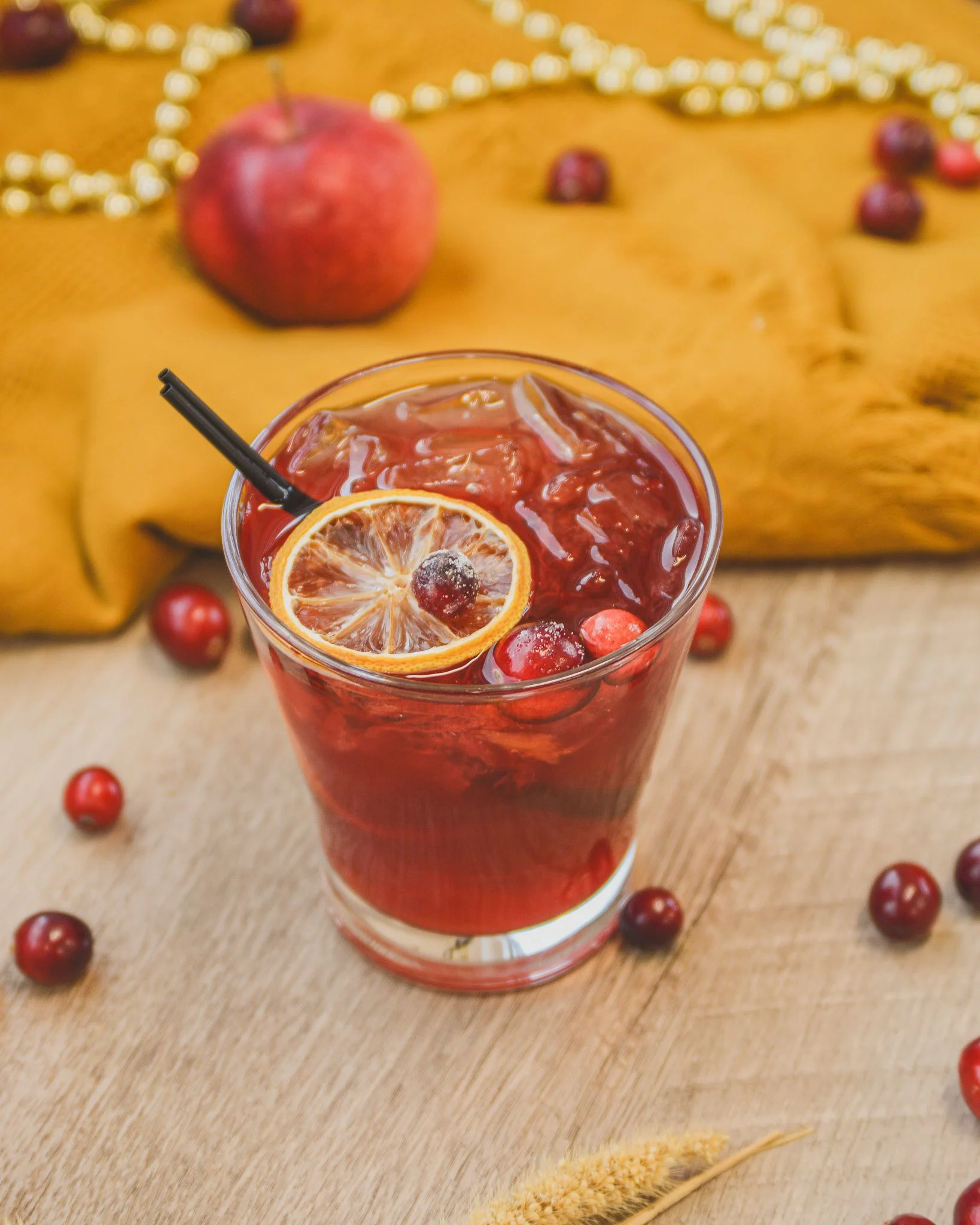 Cranberry Old Fashioned on a tabletop with cranberries and apples surrounding the cocktail
