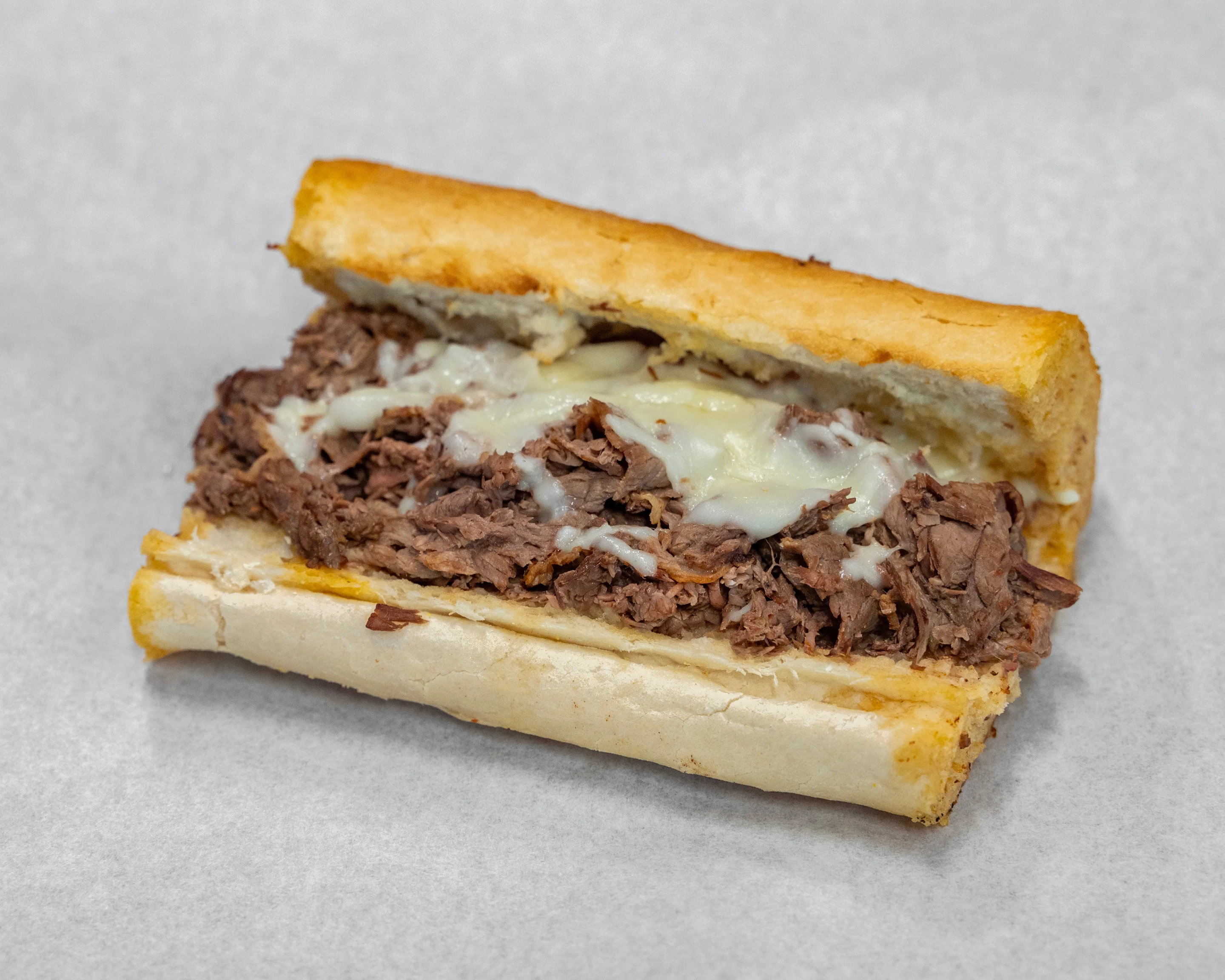 A close-up of a beef sandwich. The sandwich features tender, shredded meat topped with melted cheese, served in a toasted roll.