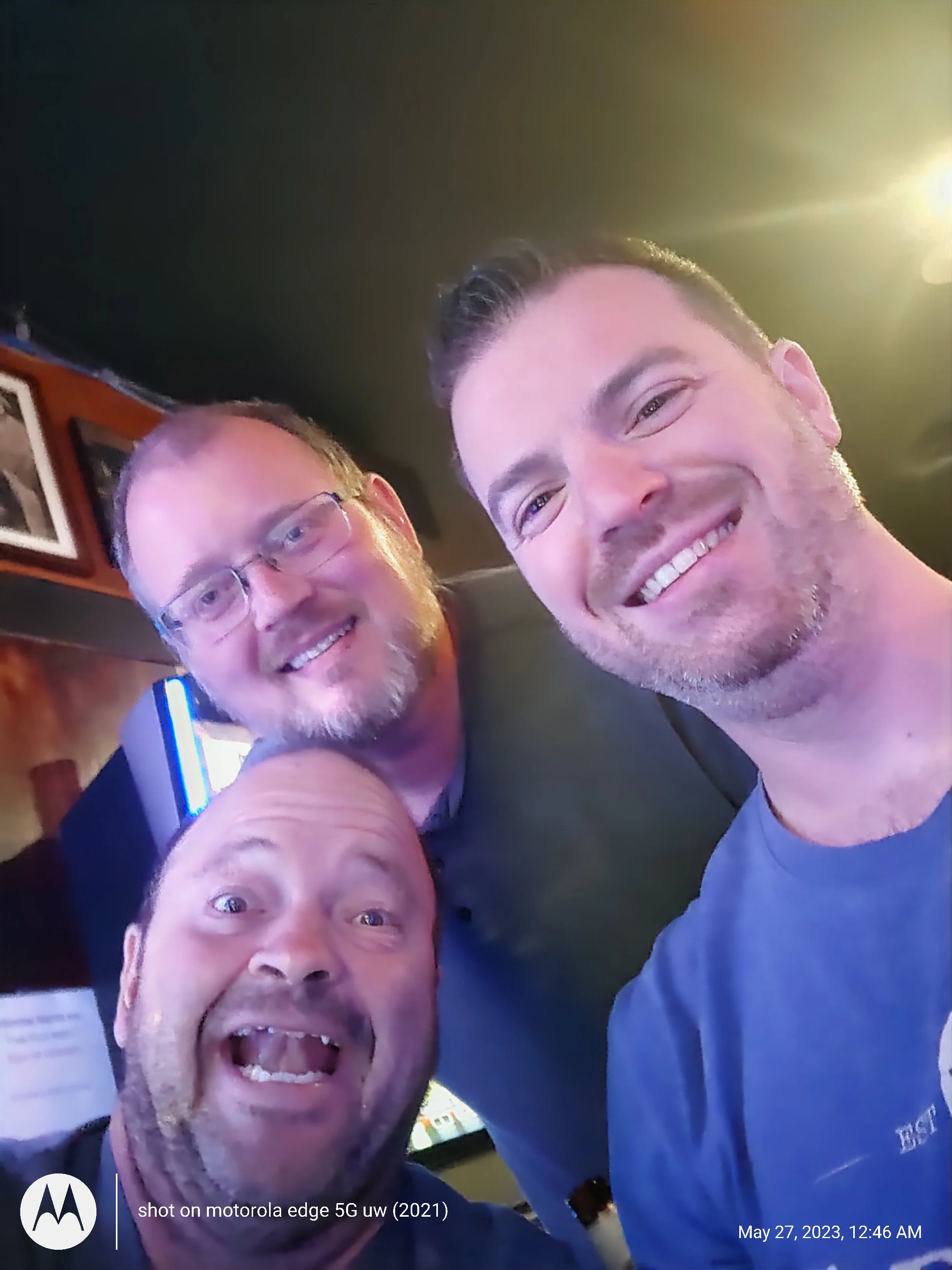 Three friends smiling for a selfie in a lively bar setting