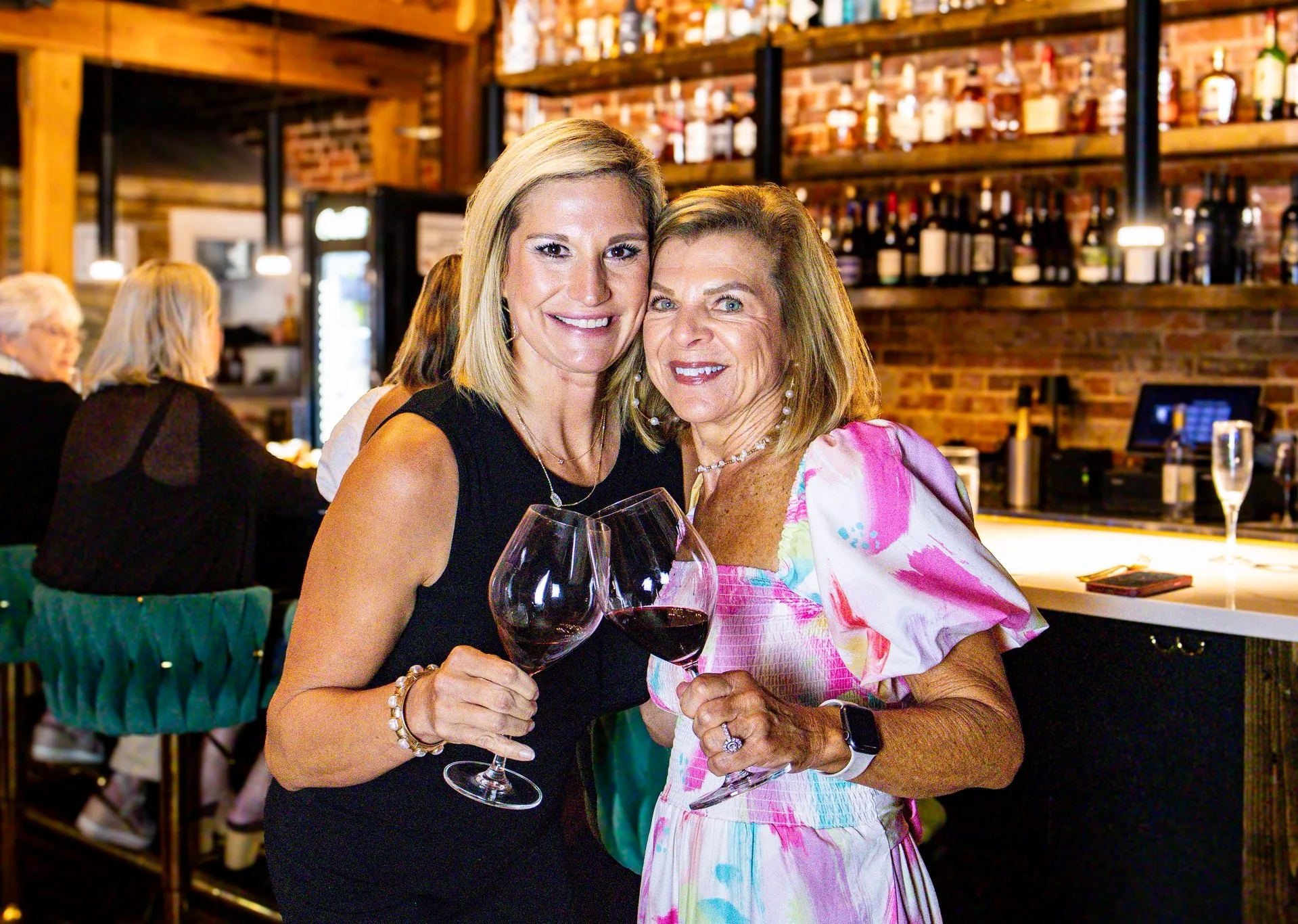 Two women toasting with red wine glasses in a cozy bar setting