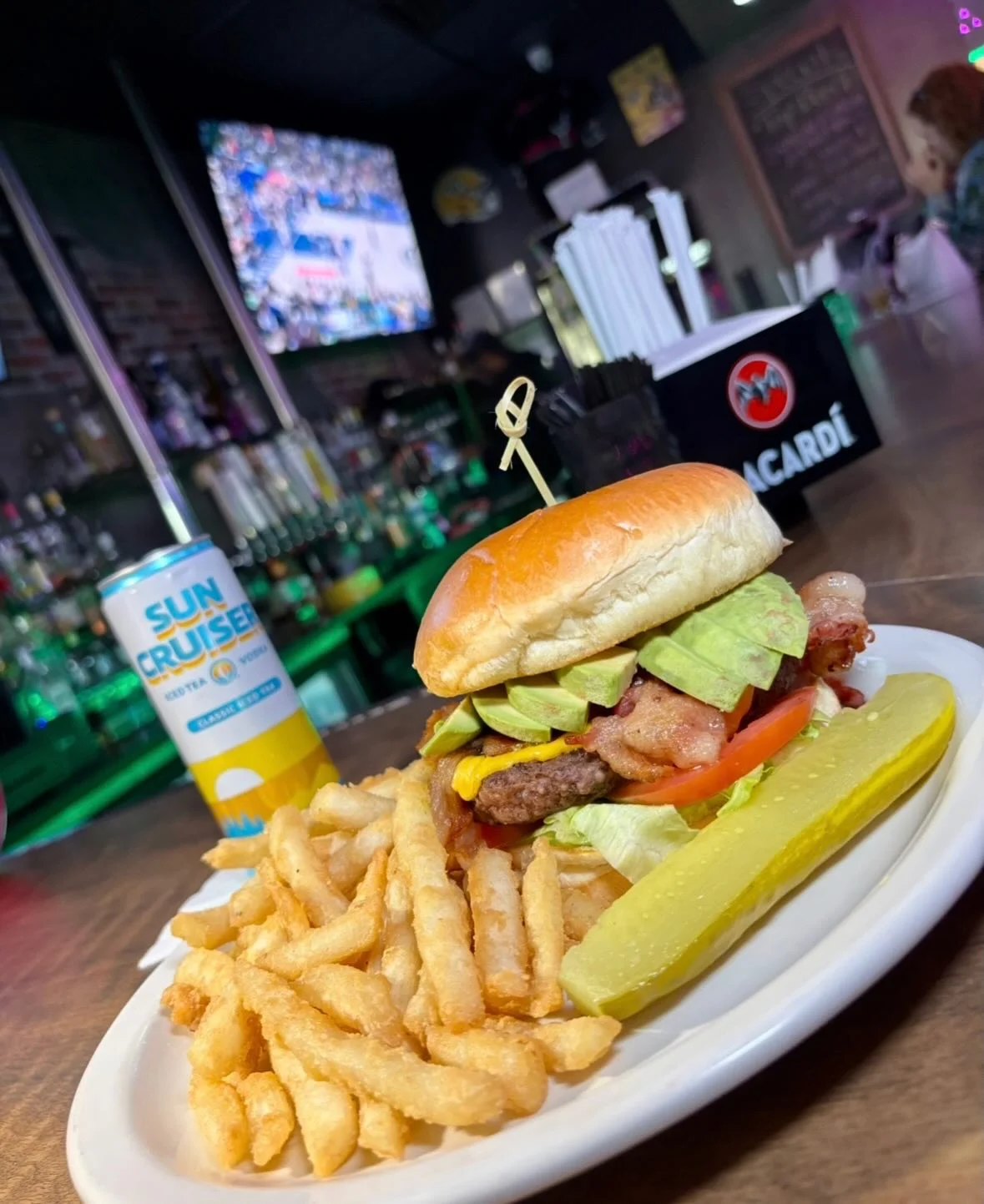 A delicious hamburger with lettuce, tomato, and bacon, served with a side of fries and a pickle.