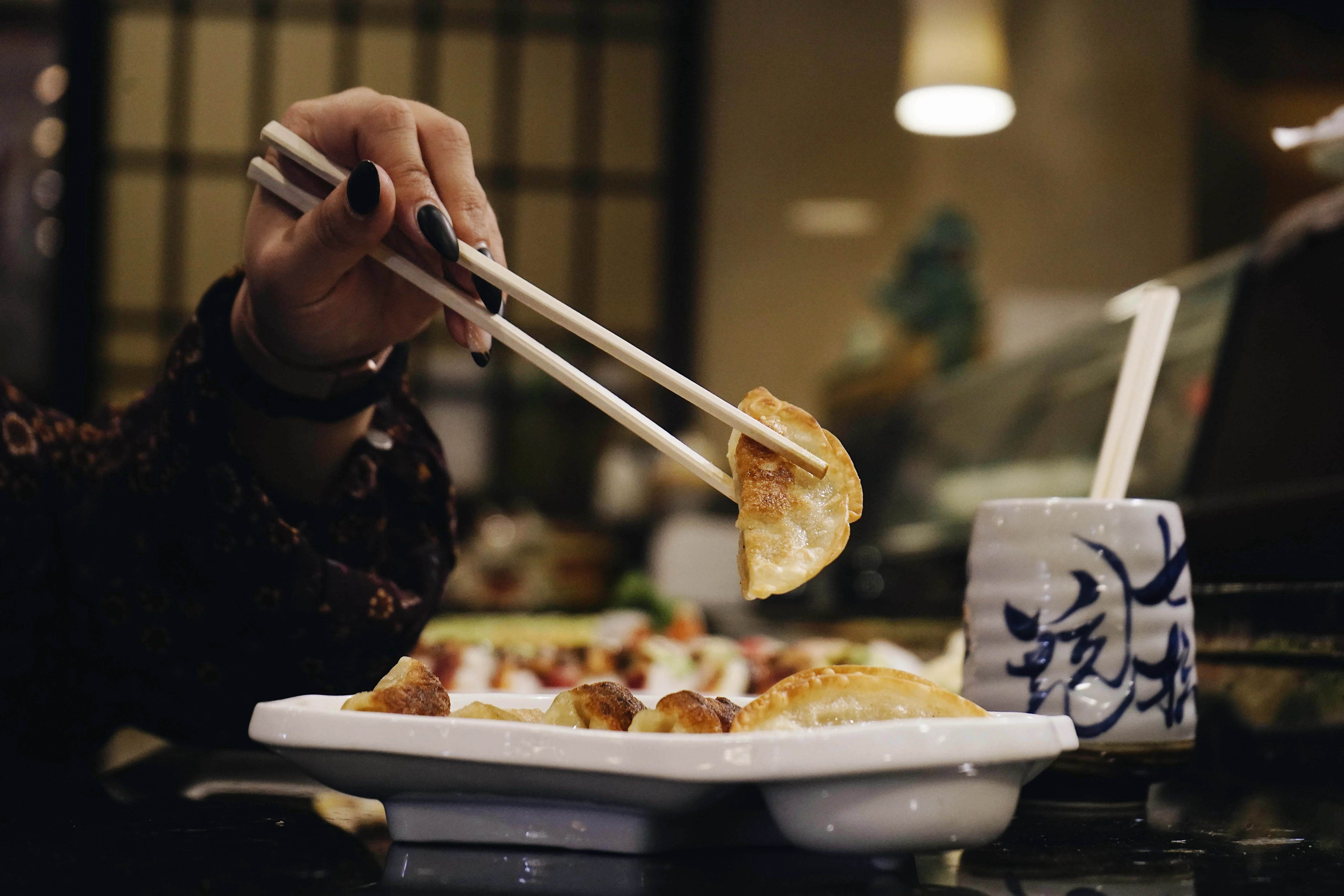 Guest lifting a gyoza dumpling with chopsticks at Mahzu East Windsor