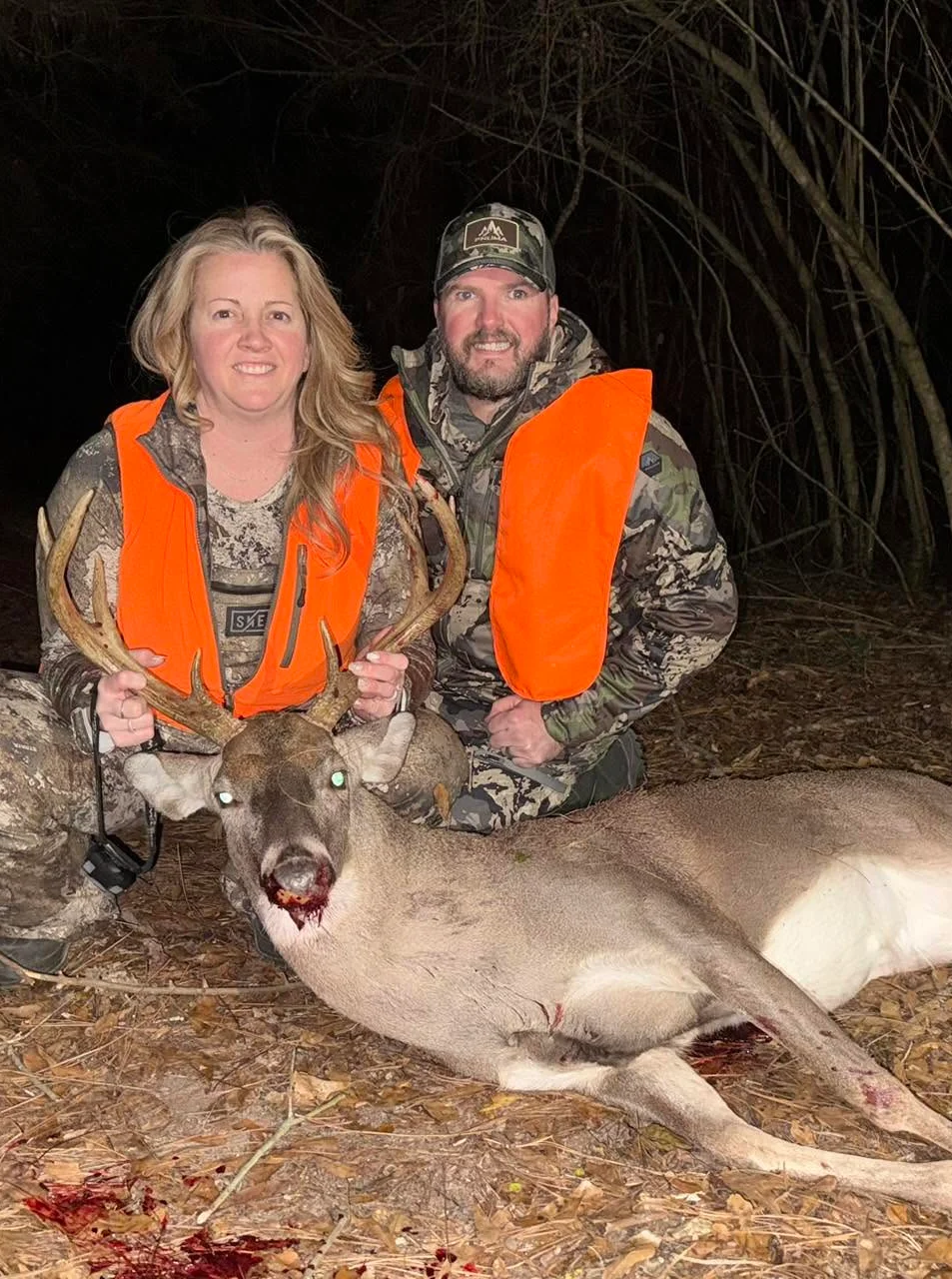 Hunters posing with a deer in a forest at night