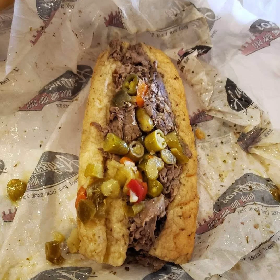 A loaded sandwich featuring tender beef, topped with pickled vegetables and served in a soft bread roll.