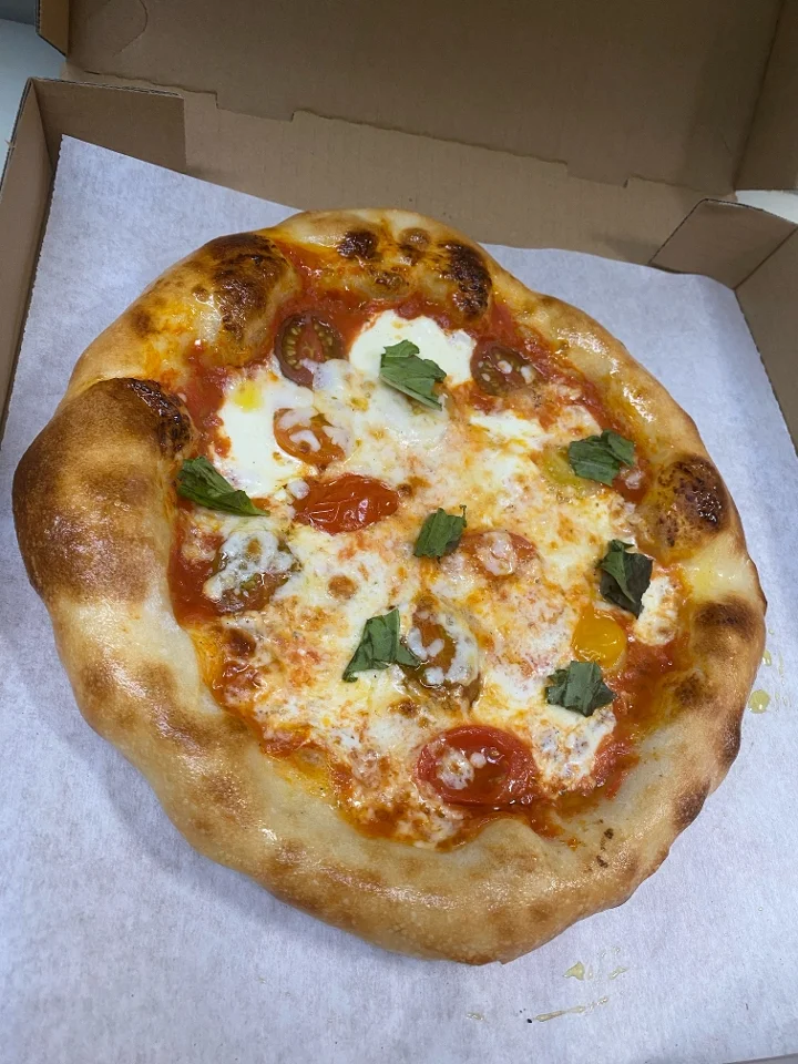 A round pizza with a golden crust, topped with fresh tomatoes and green basil leaves. The cheese is melted and bubbly.