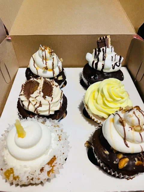 A box with six assorted cupcakes, each decorated uniquely with icing and toppings, showcasing various flavors.