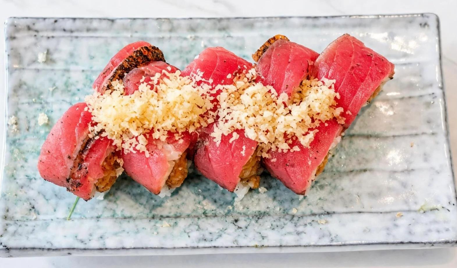 Japanese sushi rolls topped with seared tuna and crispy garlic