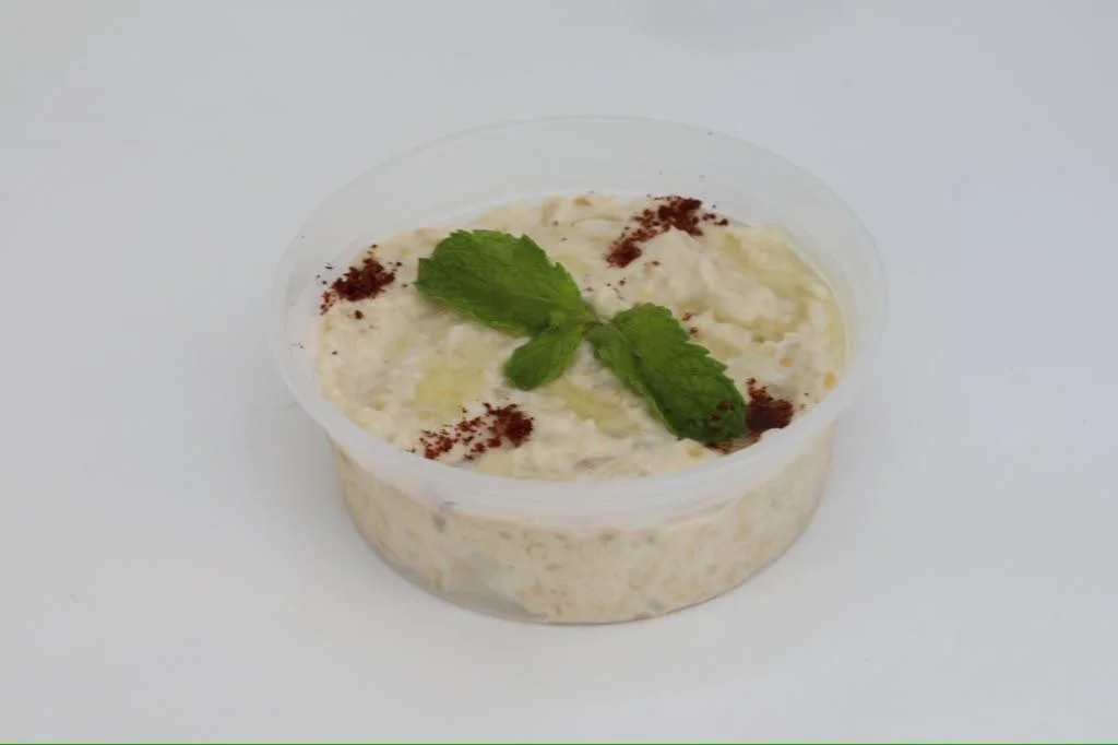 A small clear cup filled with a creamy mixture, topped with mint leaves and a sprinkle of cinnamon.