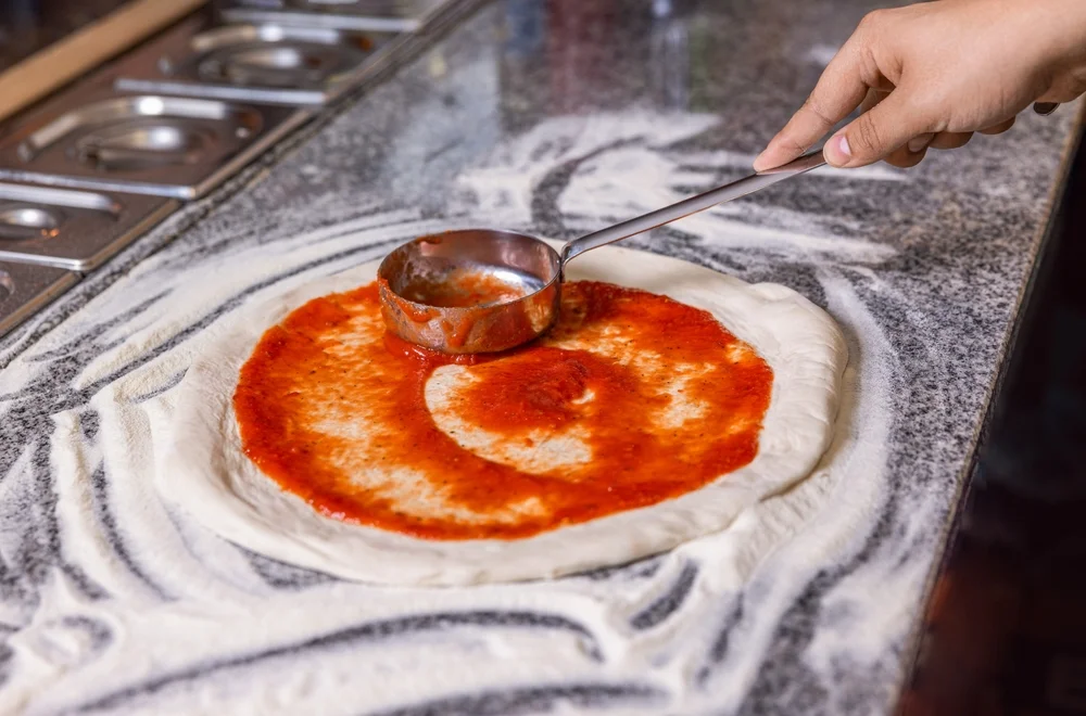 Spreading tomato sauce on pizza dough