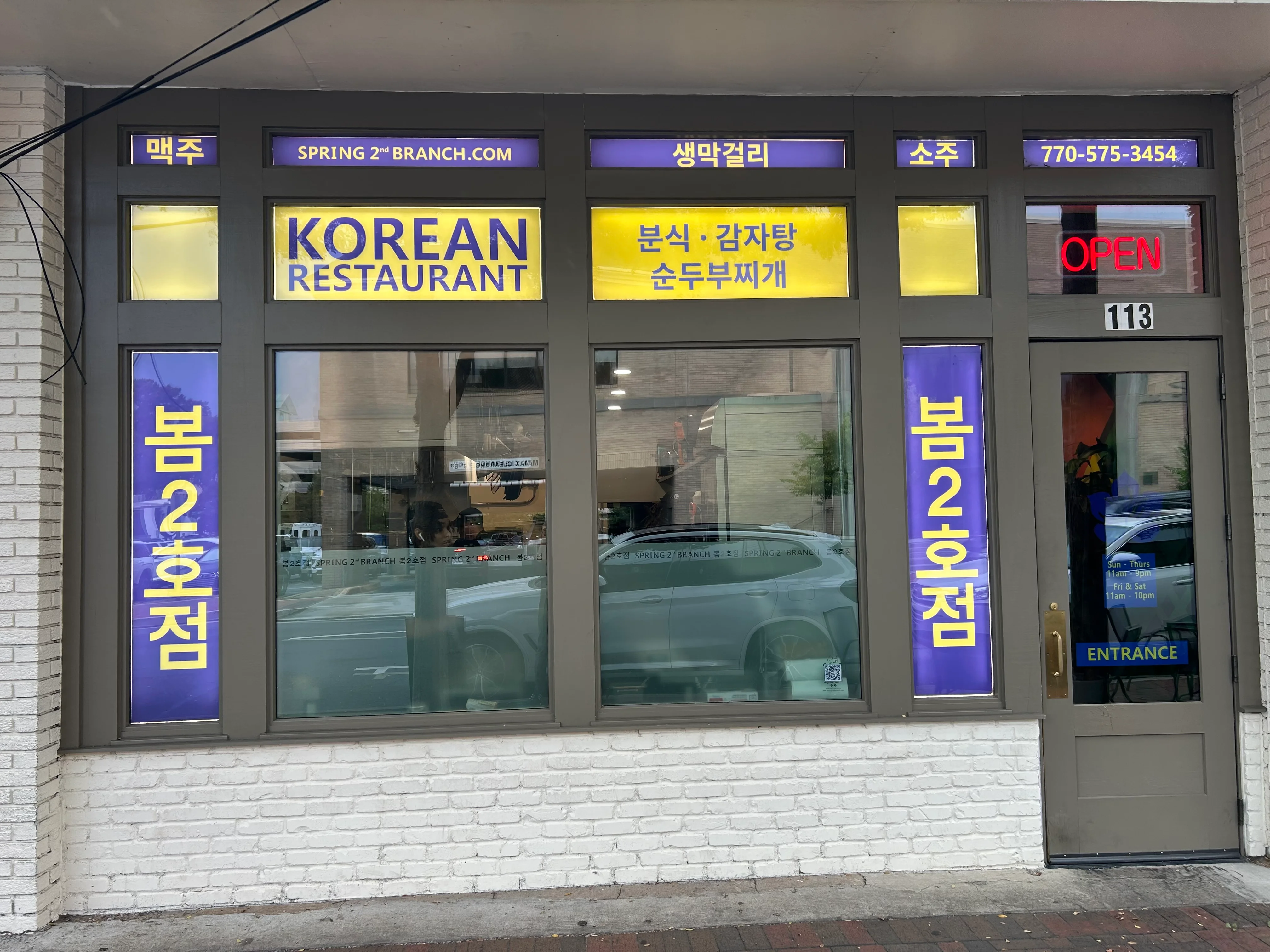 Exterior view of a Korean restaurant with vibrant signage and open hours displayed