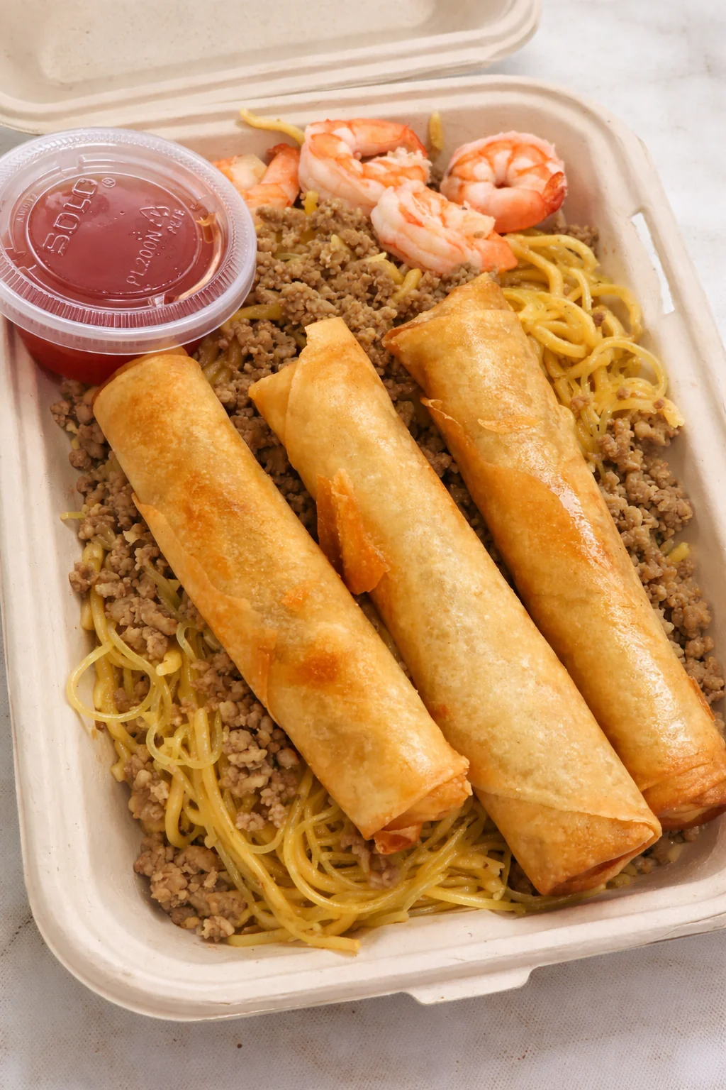 A mixed plate with fried rolls, shrimp, and a bed of seasoned noodles and ground meat, served with dipping sauce.