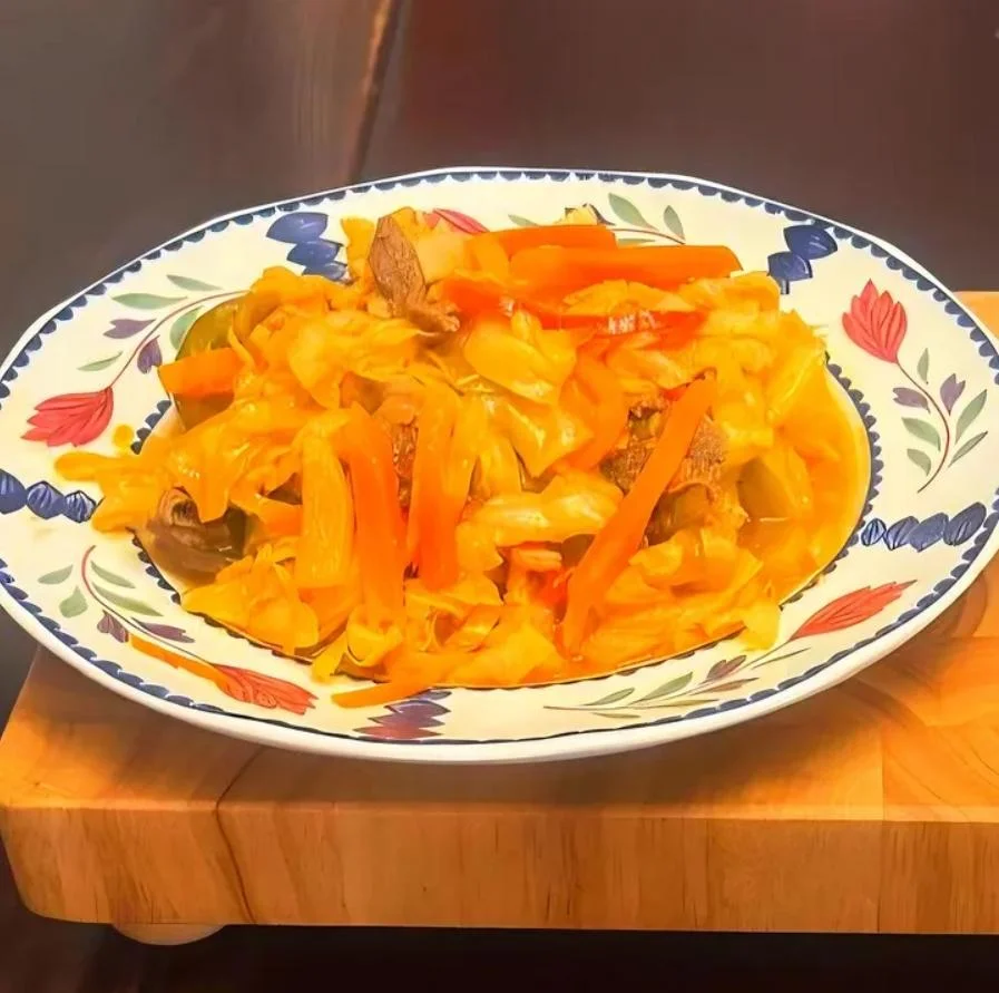 A plate of sautéed cabbage with colorful bell peppers and pieces of meat, beautifully arranged in a decorative bowl.