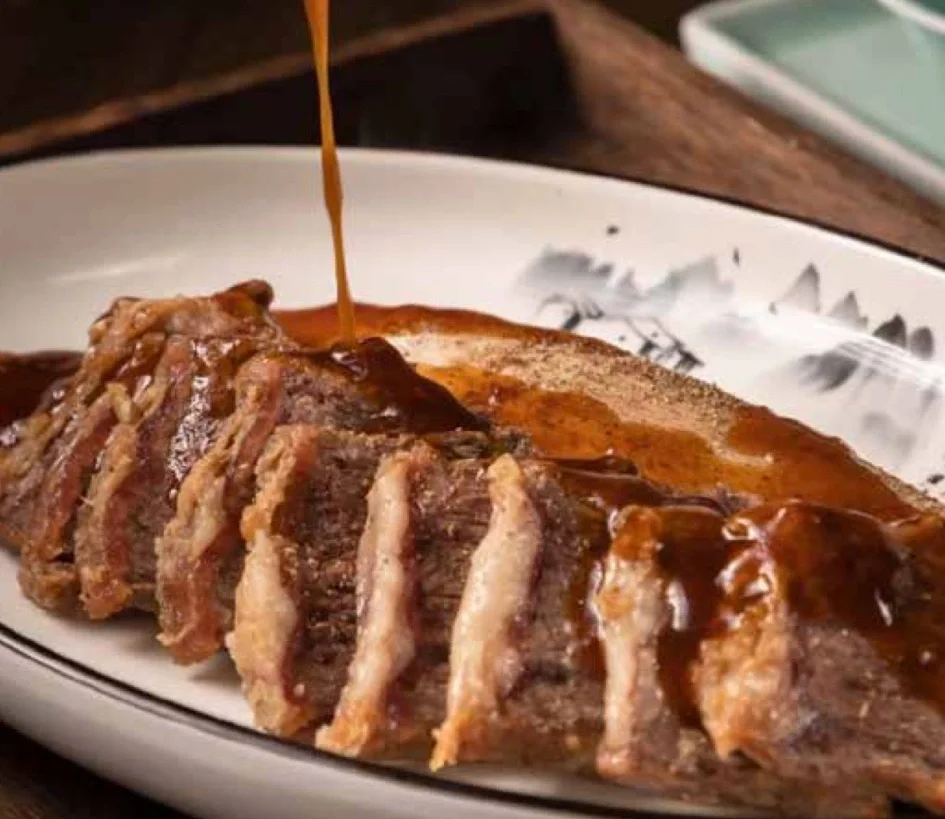Sliced beef brisket with savory sauce on a white plate