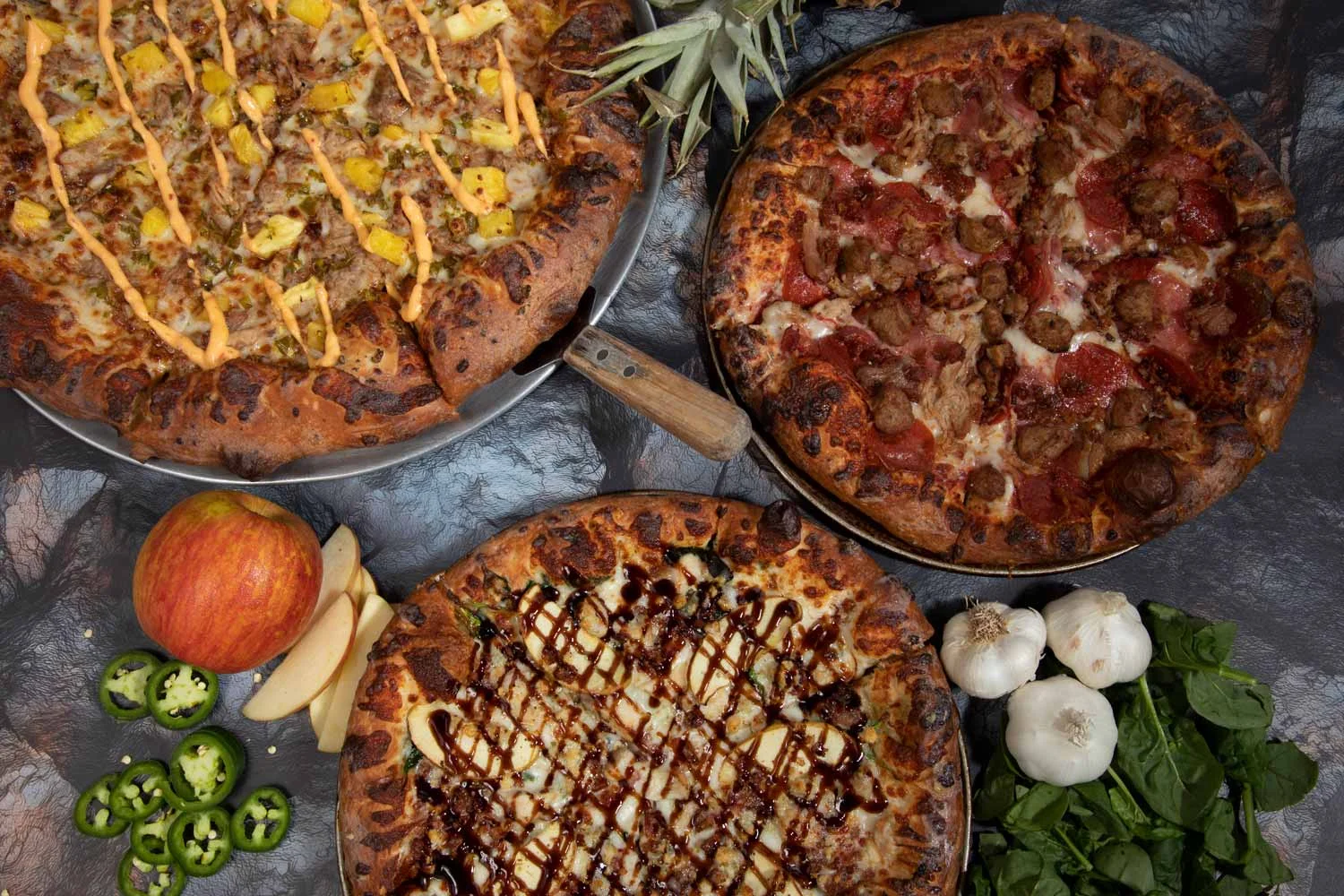 Three gourmet pizzas with unique toppings on a rustic table