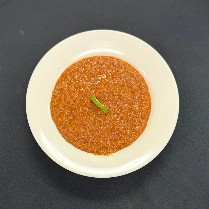 A rich red sauce with a hint of green garnish, presented on a white plate.
