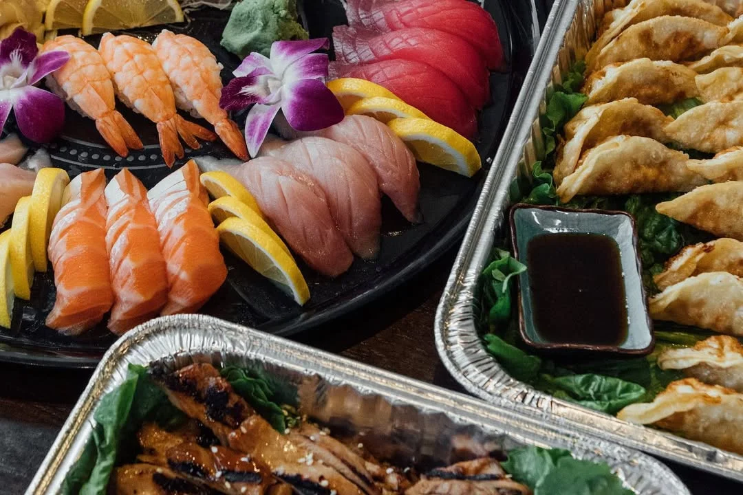 An assortment of sushi and dumplings presented beautifully on trays, featuring vibrant colors and garnishes.
