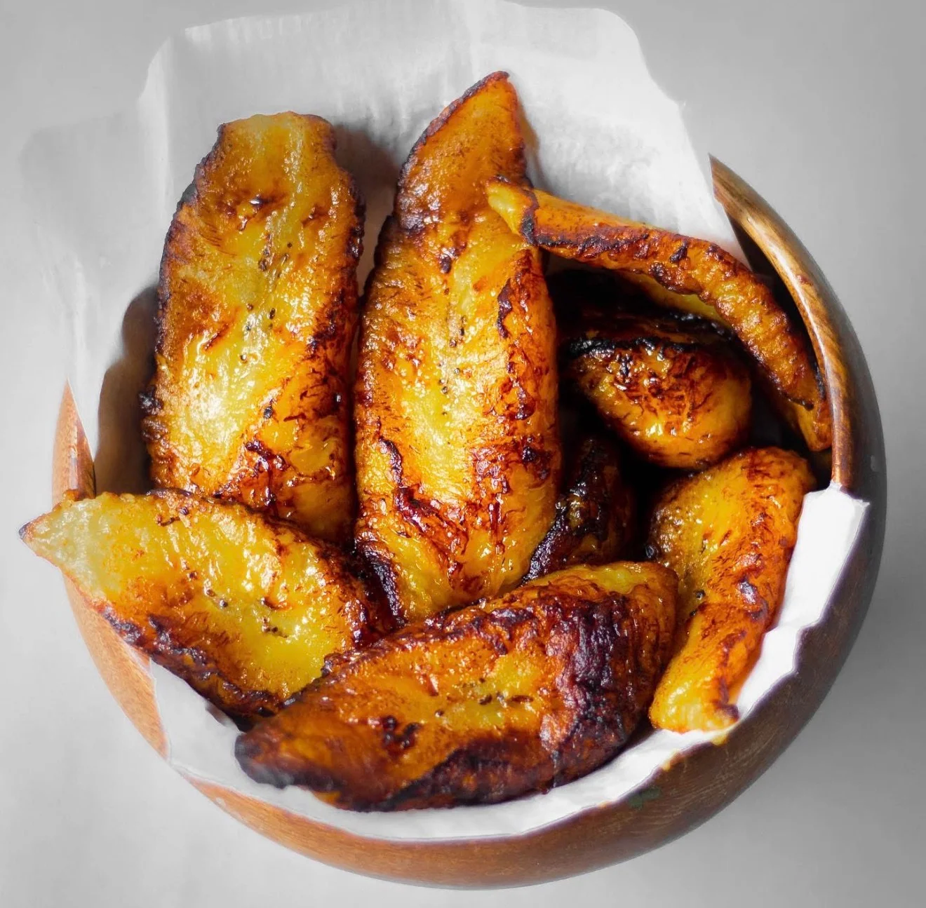 A wooden bowl filled with fried plantains, showcasing their golden-brown color and crispy texture.