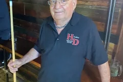 Friendly staff member at a rustic bar with a pool cue