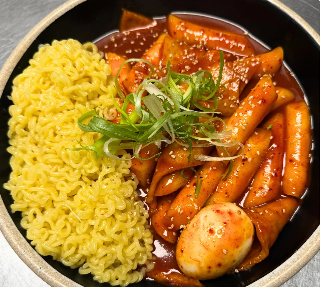 A bowl of tteokbokki with ramen and a boiled egg, garnished with green onions.