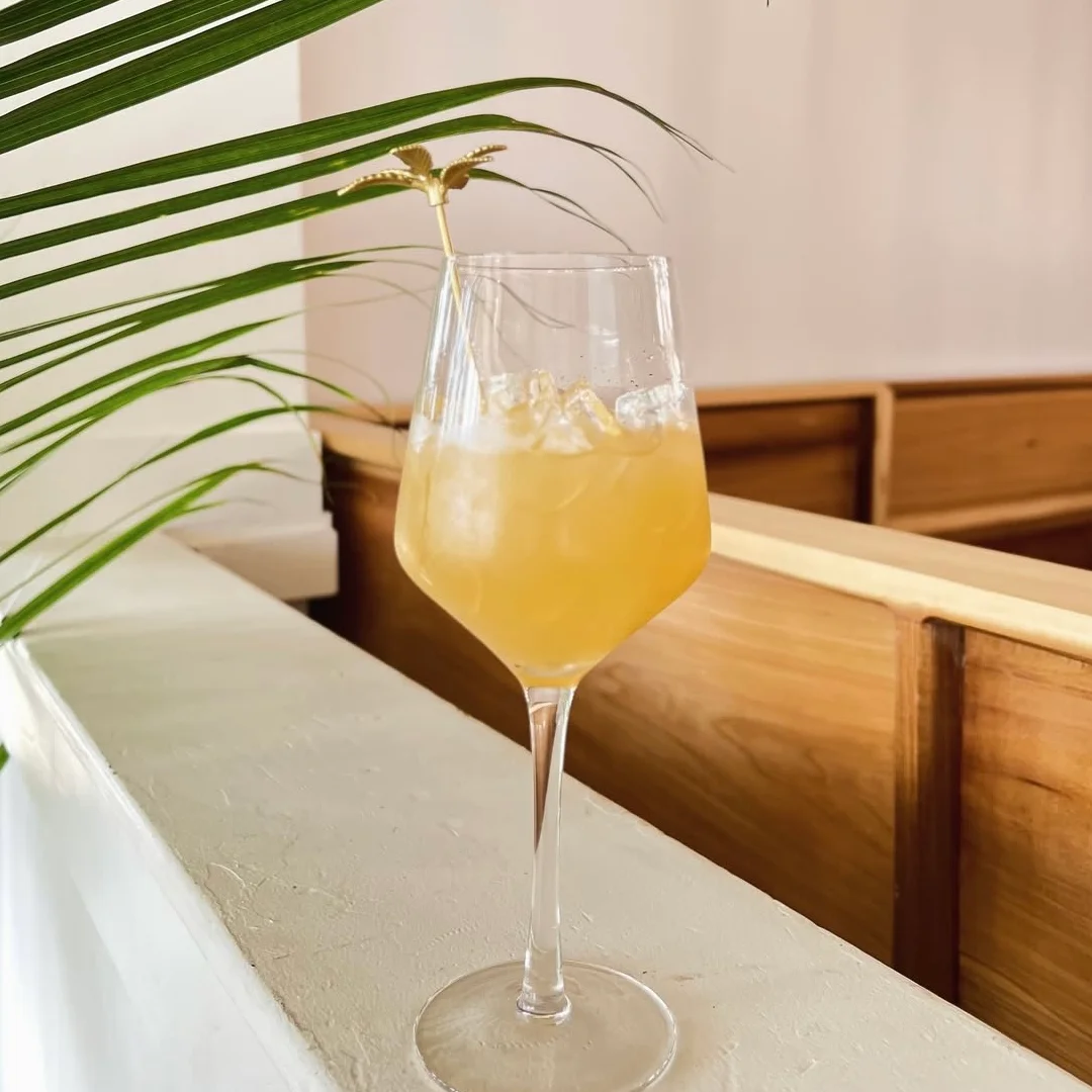 A refreshing yellow cocktail served in a glass with ice and a decorative stirrer.