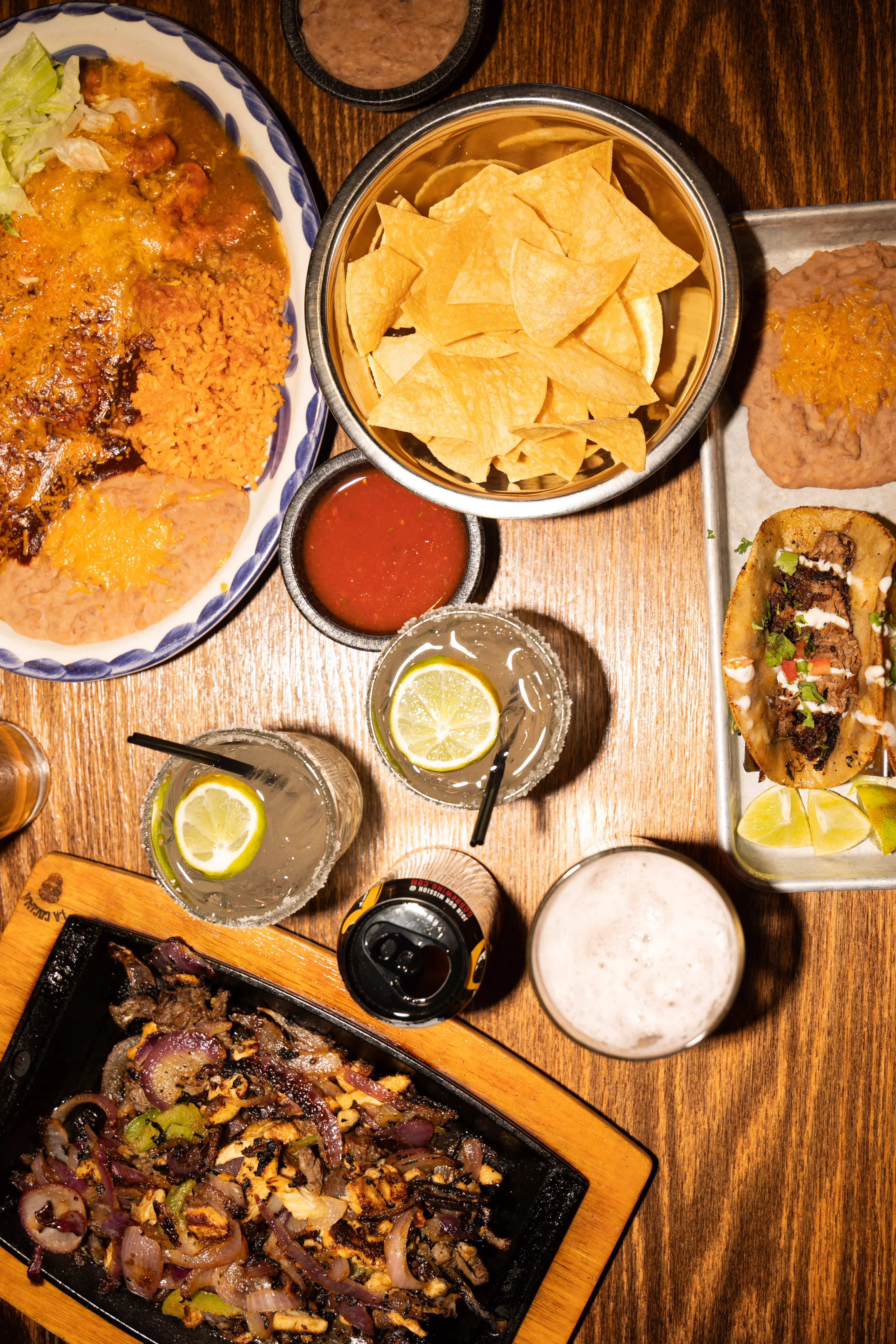 Colorful Mexican feast with tacos, chips, and drinks on a wooden table