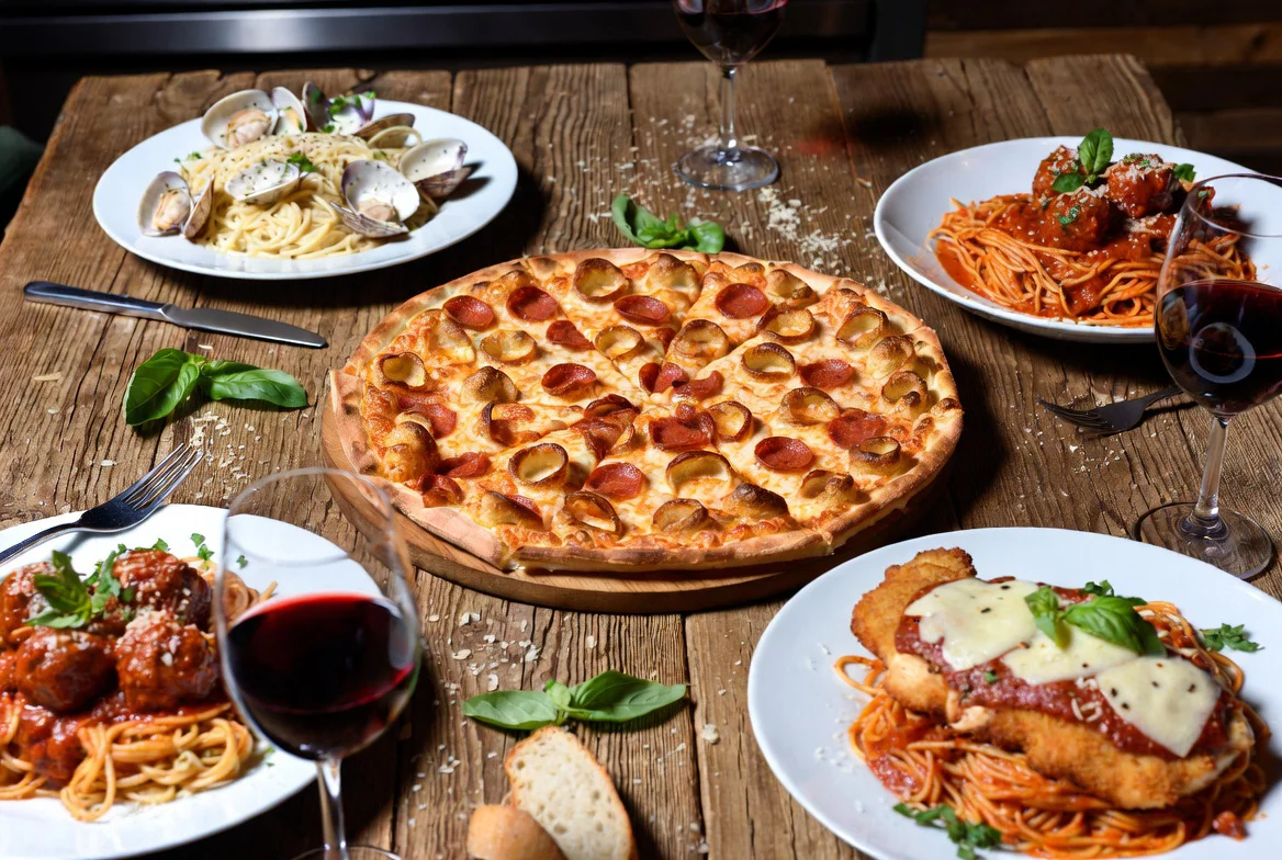 A table with various Italian dishes including pizza, pasta, and wine.