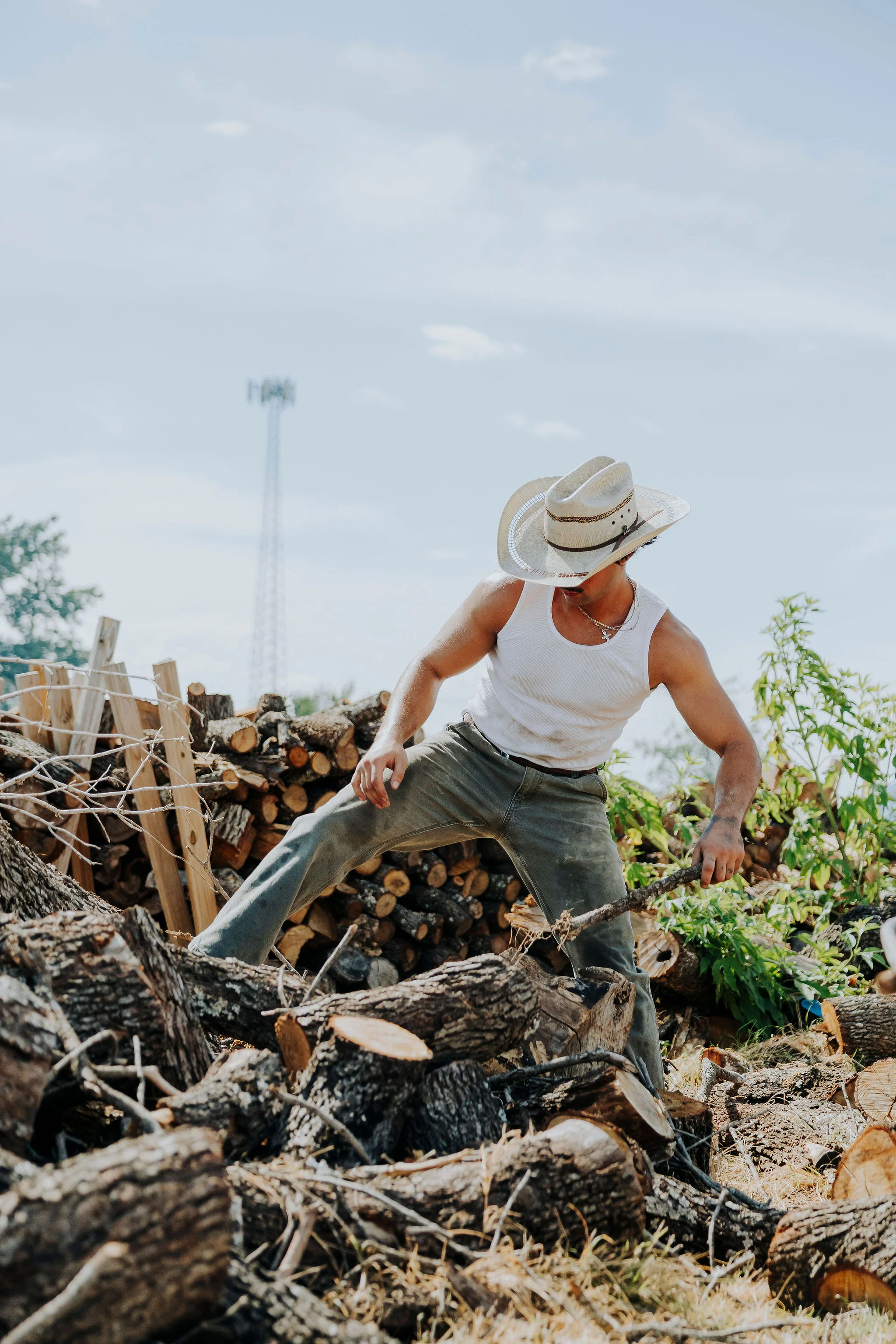 Man in a cowboy hat working with firewood outdoors