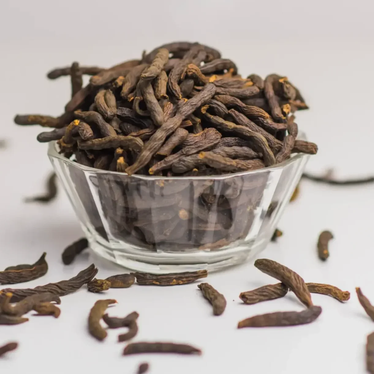 A glass bowl filled with dried, dark brown herbs or spices.