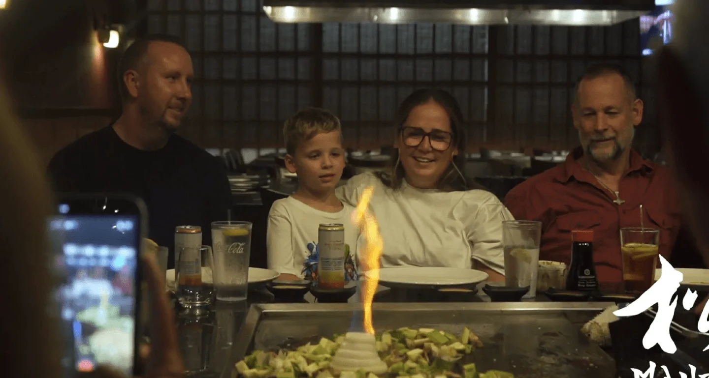 Family at a hibachi table with a drink in hand as the onion volcano flames at Mahzu East Windsor, BYOB
