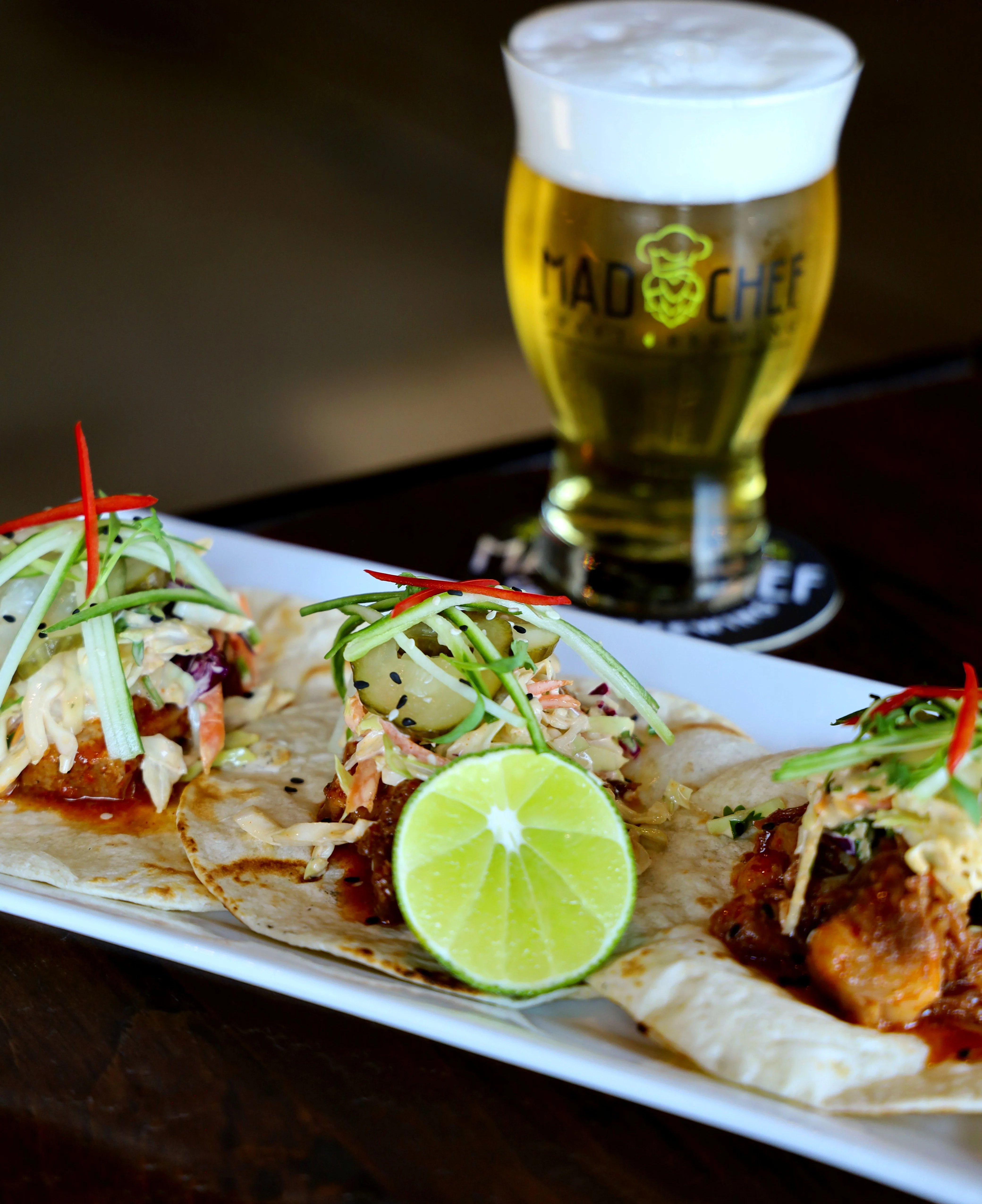 Three tacos with pulled meat, pineapple, and lime on a plate.