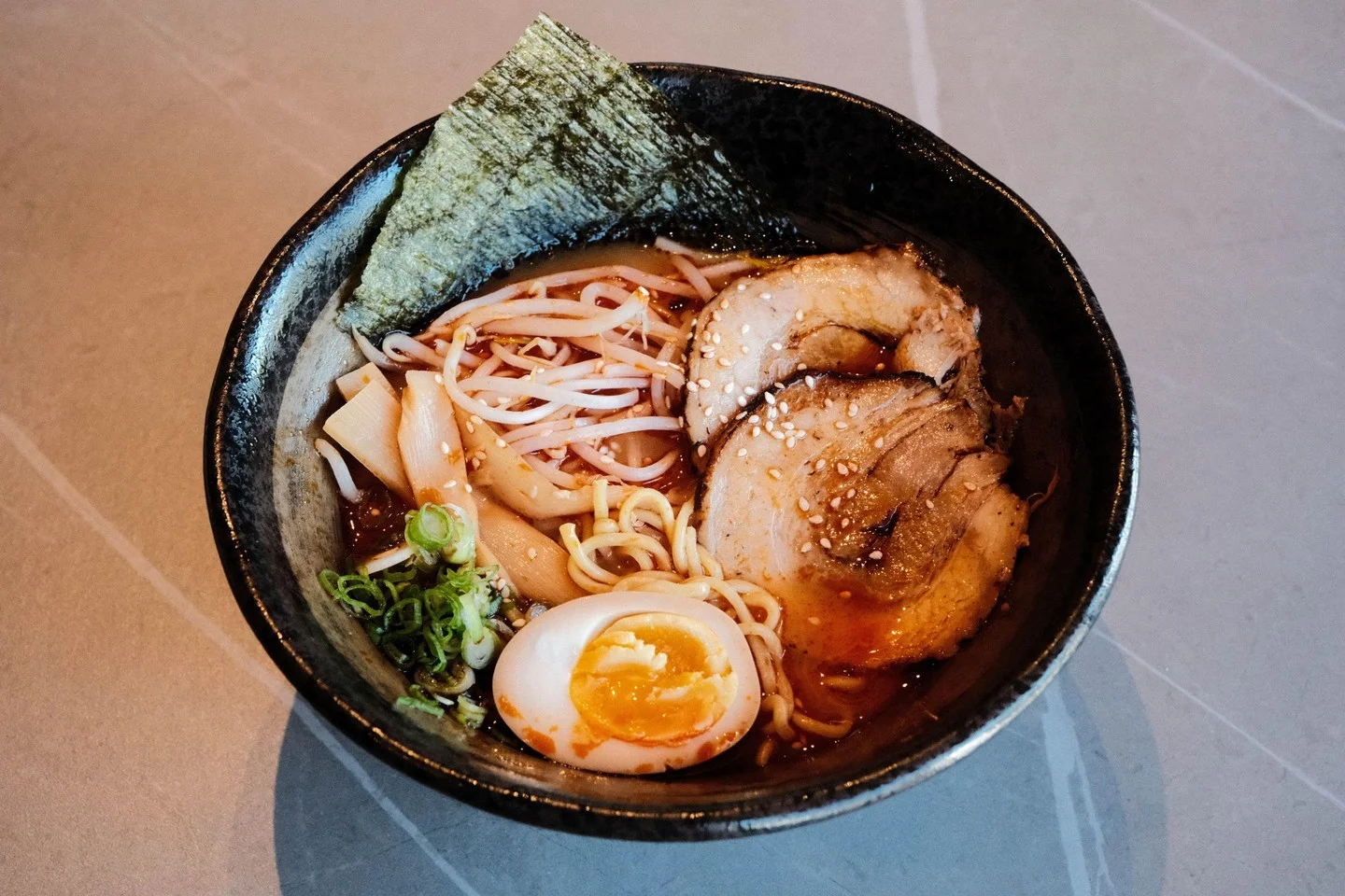 A bowl of ramen featuring noodles, slices of meat, a soft-boiled egg, and garnished with seaweed and sesame seeds.