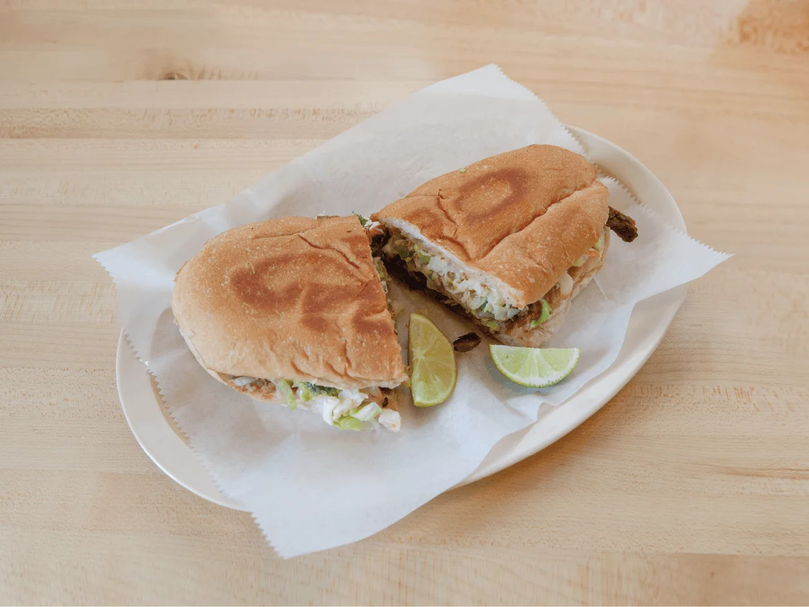 Delicious Mexican torta with fresh toppings and lime wedges