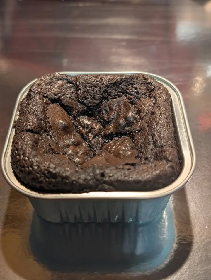 A rich, dark chocolate dessert baked in a metal container, featuring a slightly cracked top.