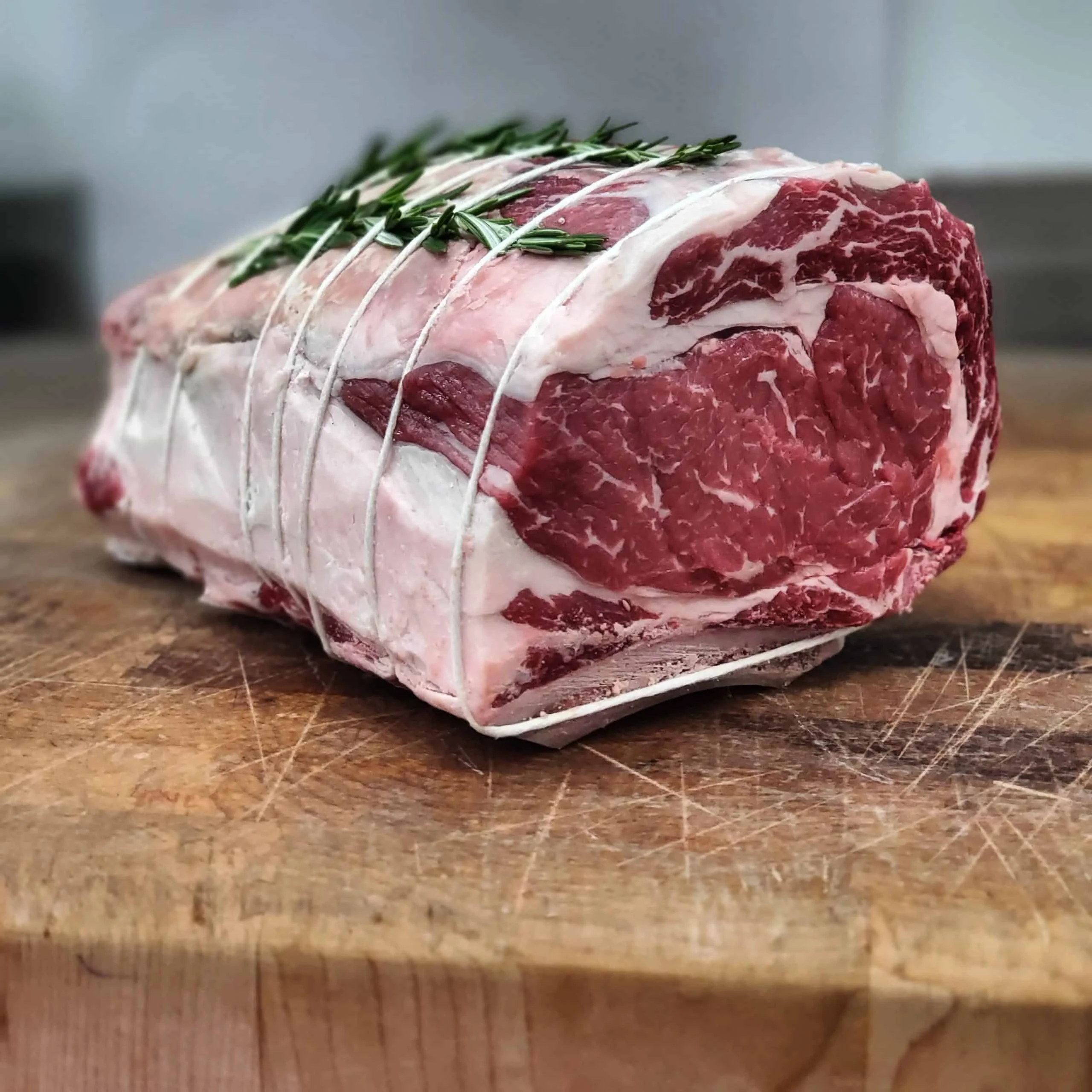 Raw beef roast with rosemary on a wooden cutting board.