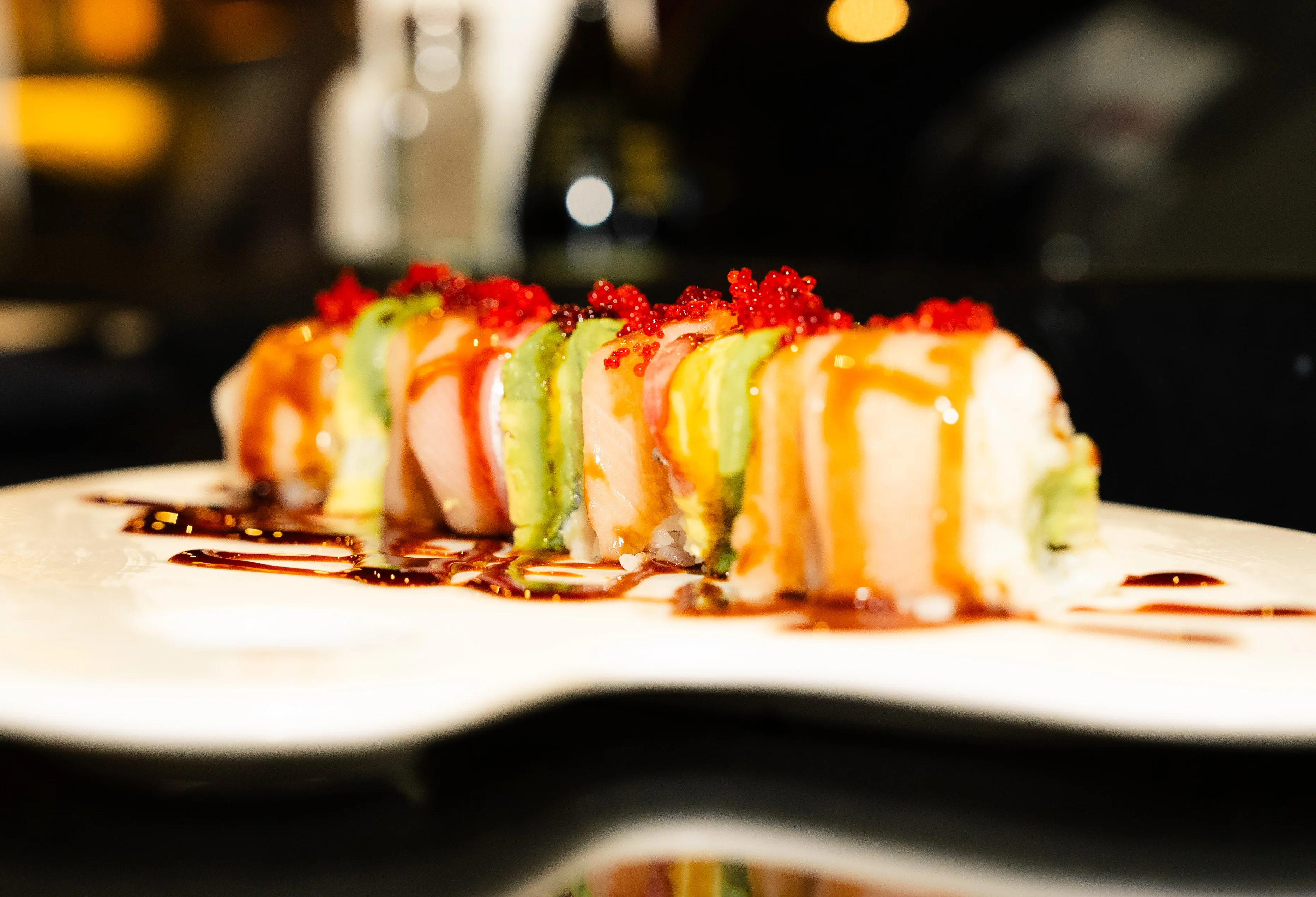 Colorful sushi rolls drizzled with sauce and topped with roe