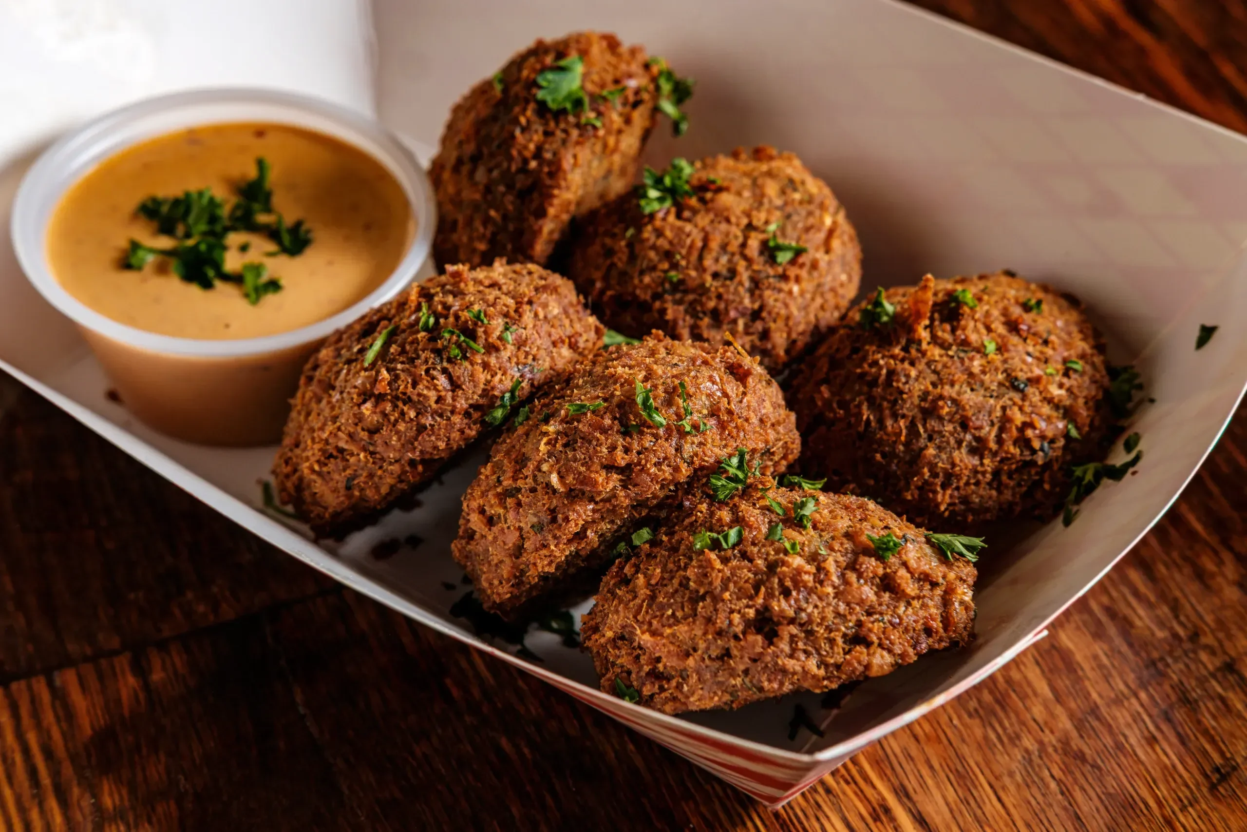 A platter of crispy fried balls accompanied by a rich dipping sauce, garnished with fresh herbs.